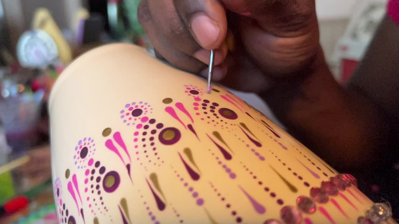 Artist carefully paints a vase with a dot art design