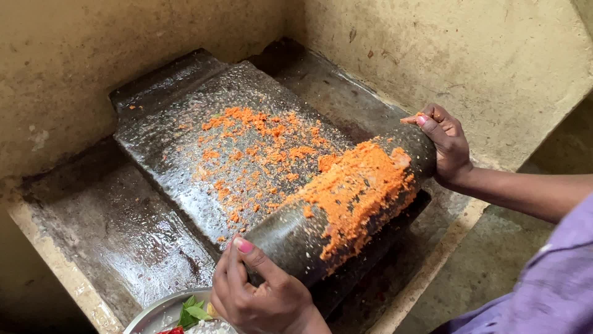 Woman preparing coconut chutney using a traditional roller stone