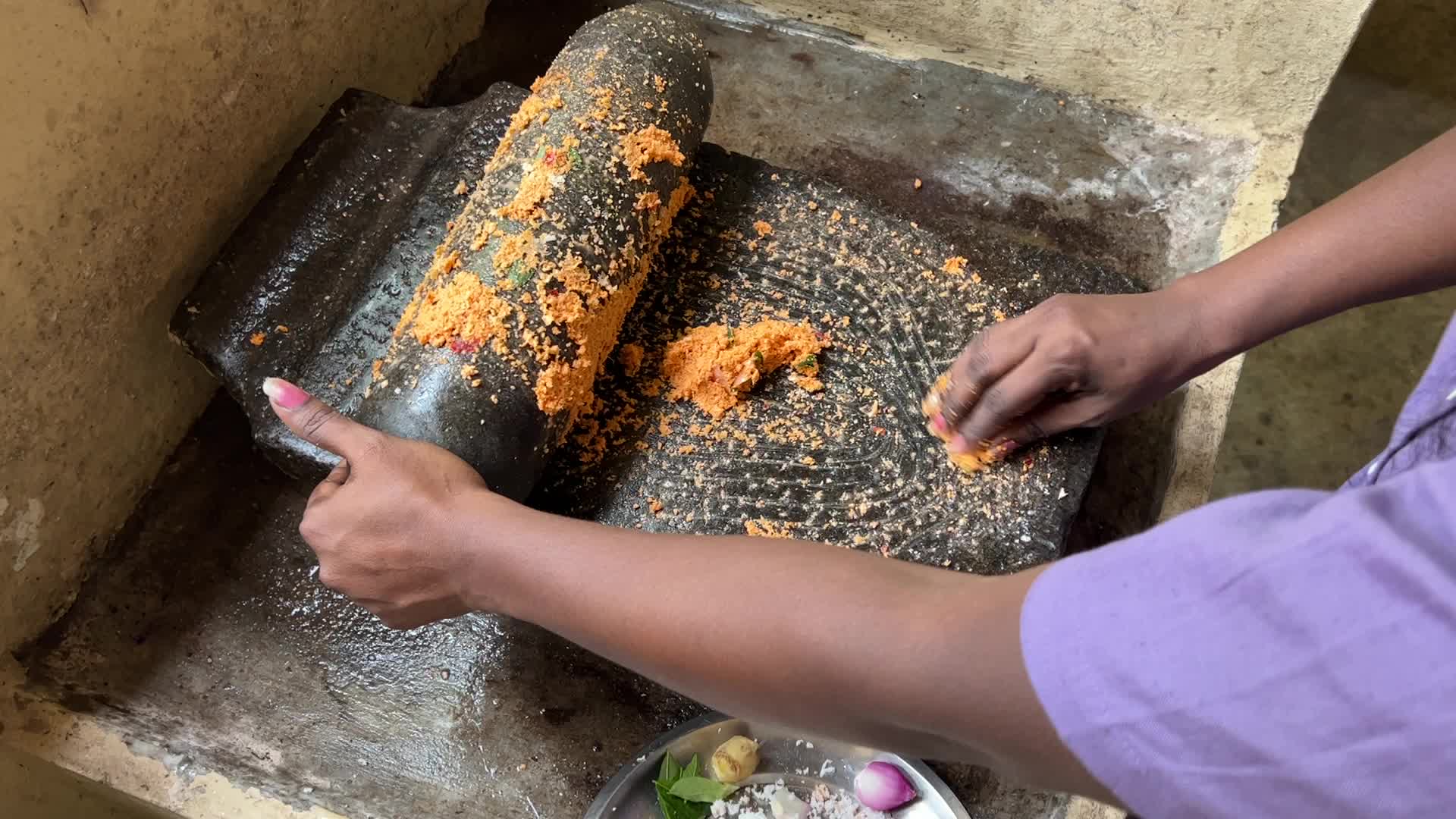 Woman preparing coconut chutney using a traditional roller stone