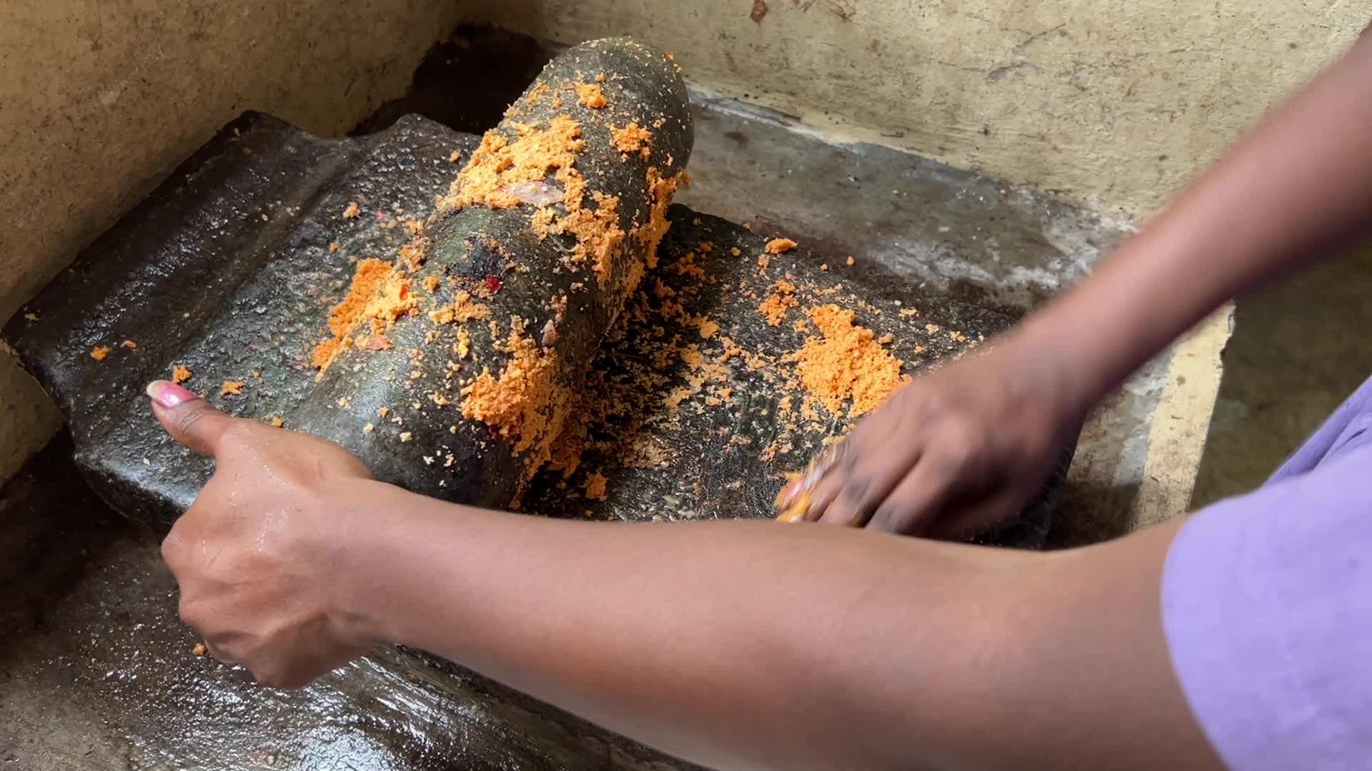Woman preparing coconut chutney using a traditional roller stone