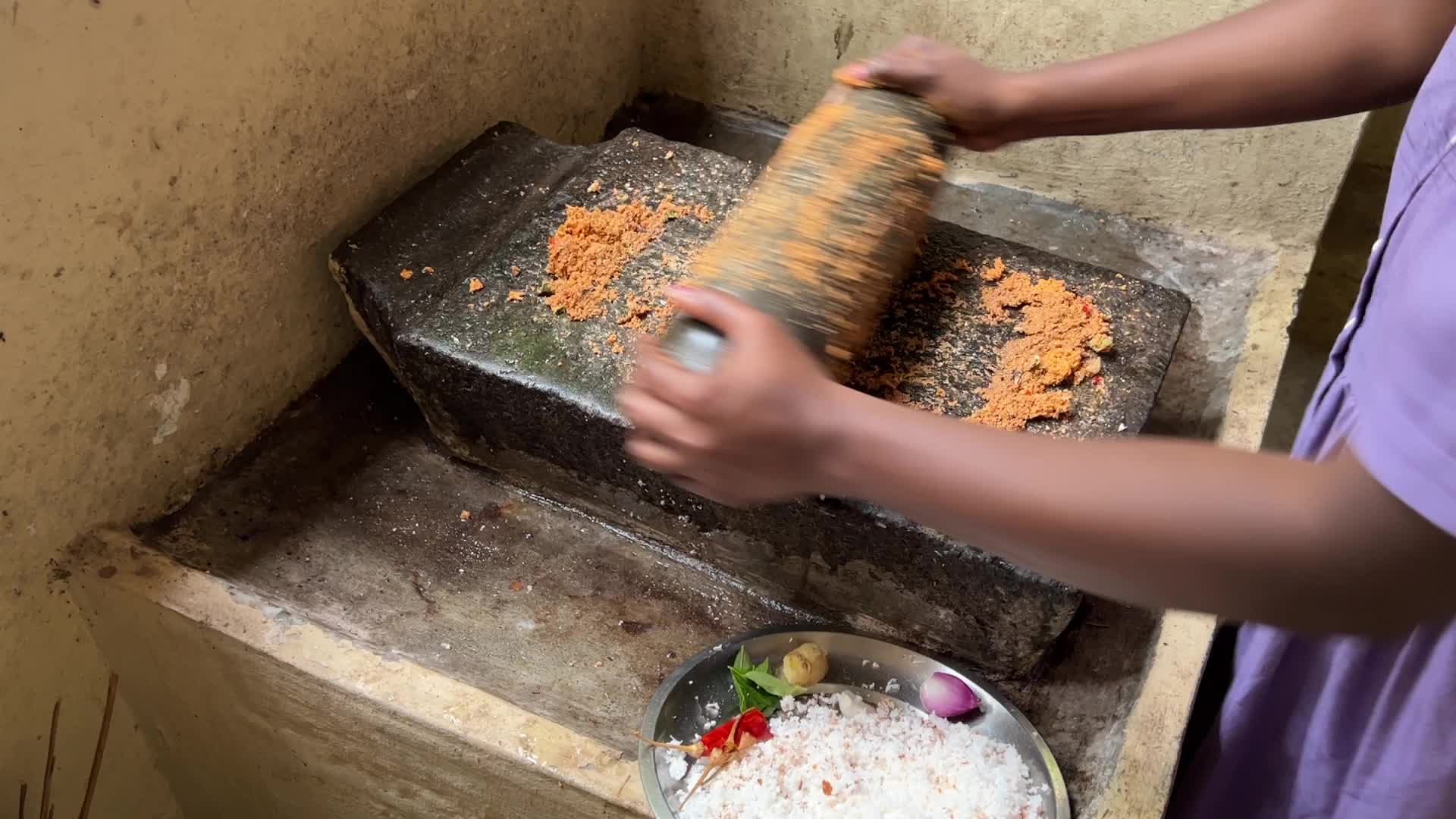 Woman preparing coconut chutney using a traditional roller stone
