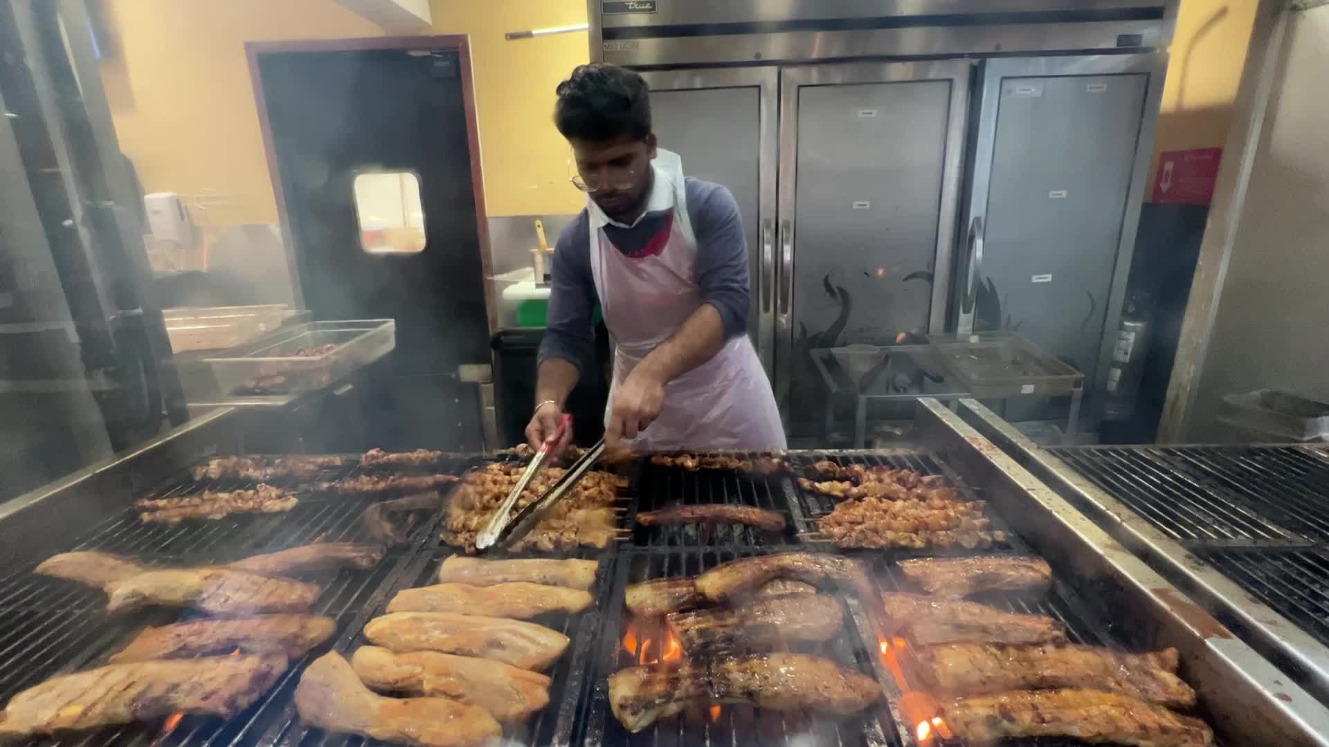Man barbecues meat on a large grill at a restaurant