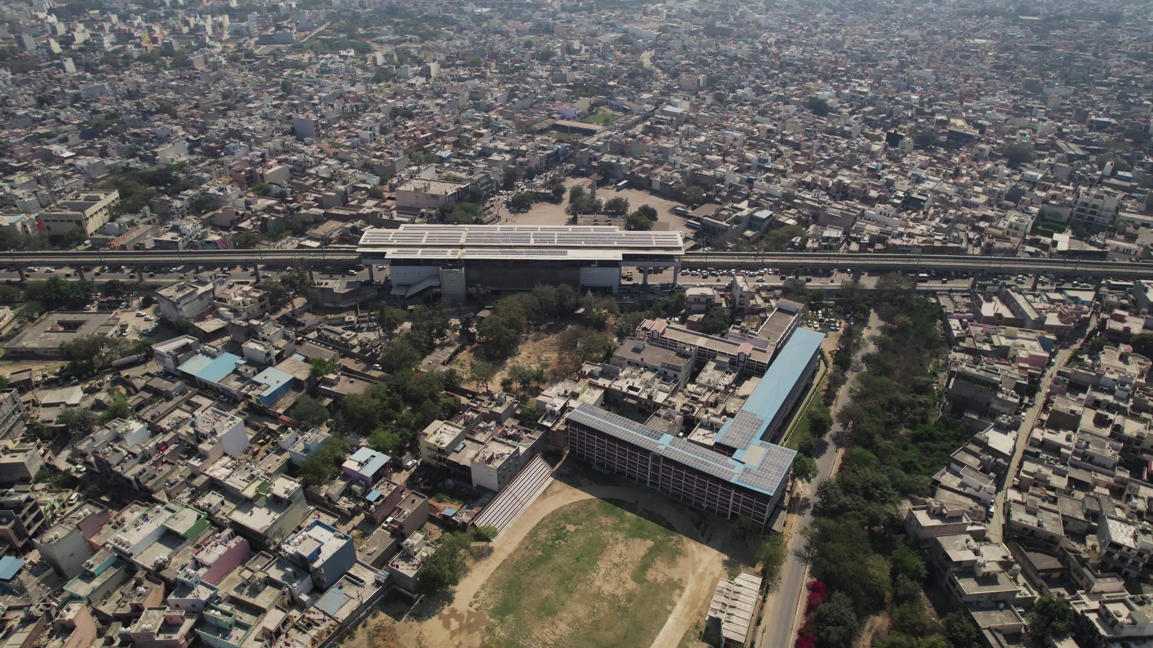 4K Aerial overpopulated View of Industrial & Residential Estate in Bahadurgarh City with elevated Metro train tracks and solar panels installed on the roof of the Metro Station, Harayana, India - stock video