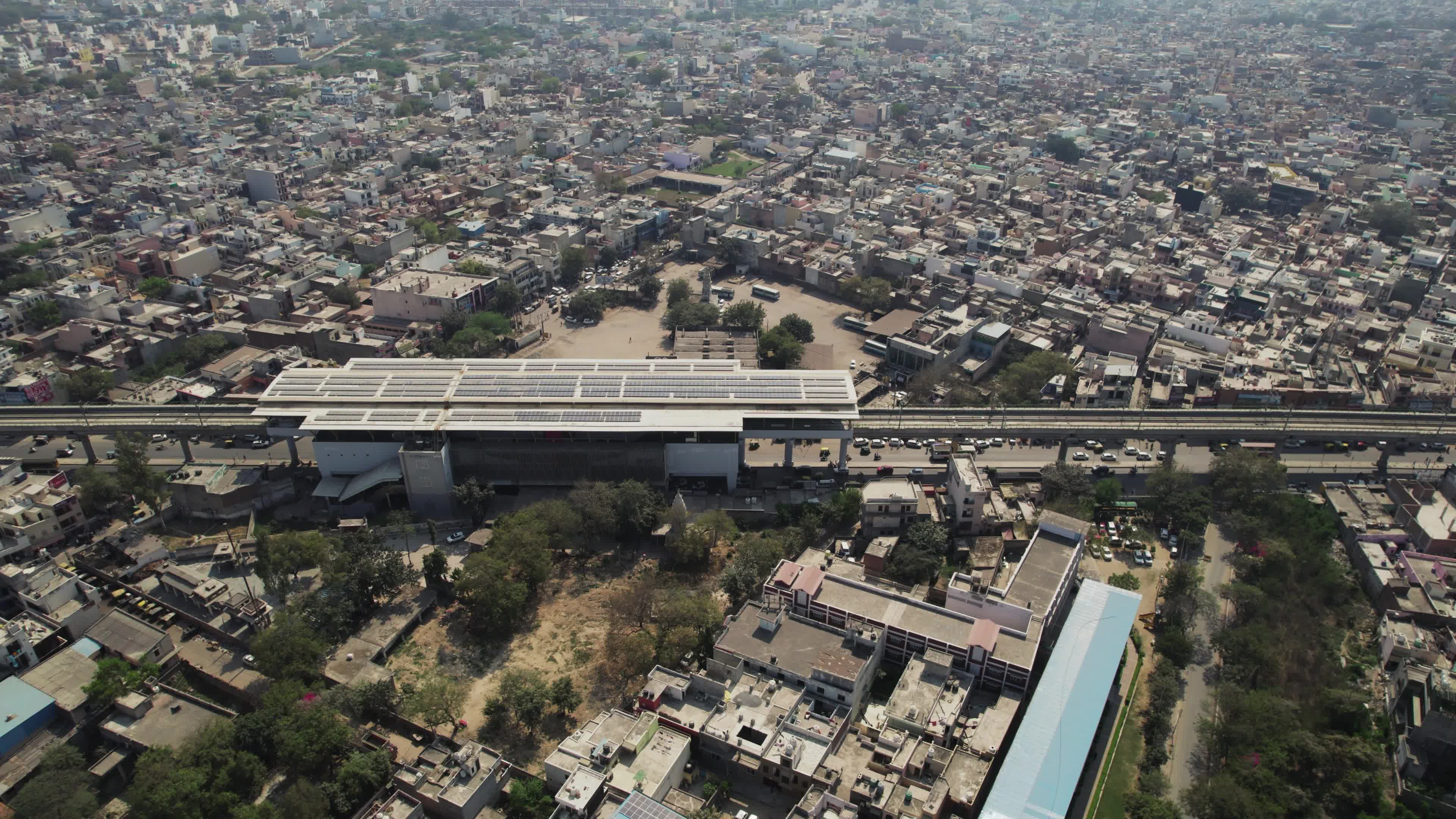 4K Aerial overpopulated View of Industrial & Residential Estate in Bahadurgarh City with elevated Metro train tracks and solar panels installed on the roof of the Metro Station, Harayana, India - stock video