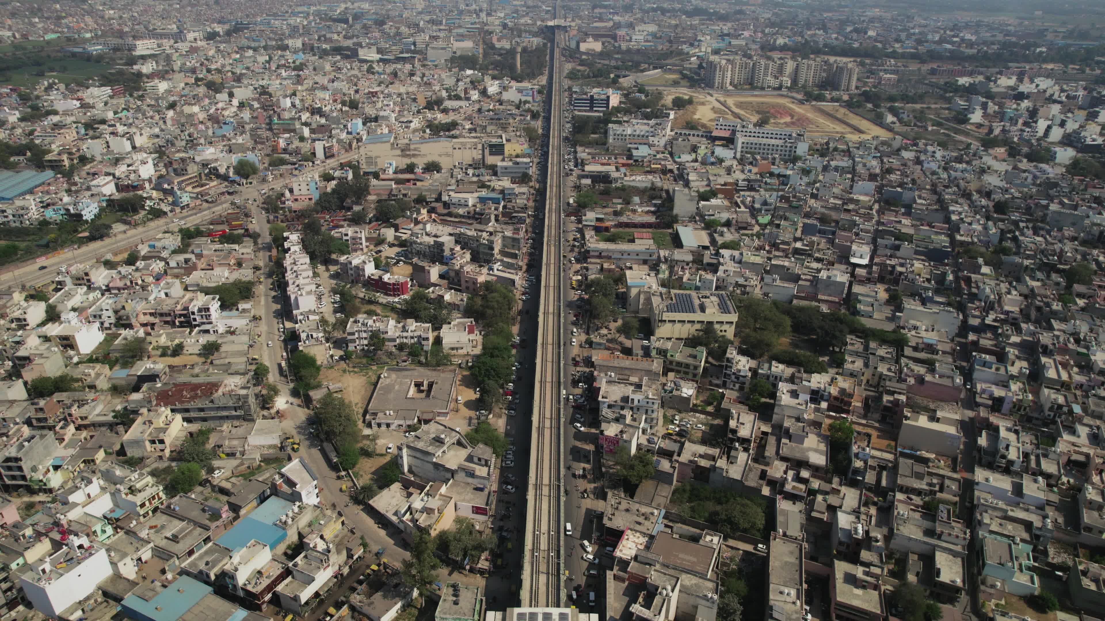 4K Aerial overpopulated View of Industrial & Residential Estate in Bahadurgarh City with elevated Metro train tracks and solar panels installed on the roof of the Metro Station, Harayana, India - stock video