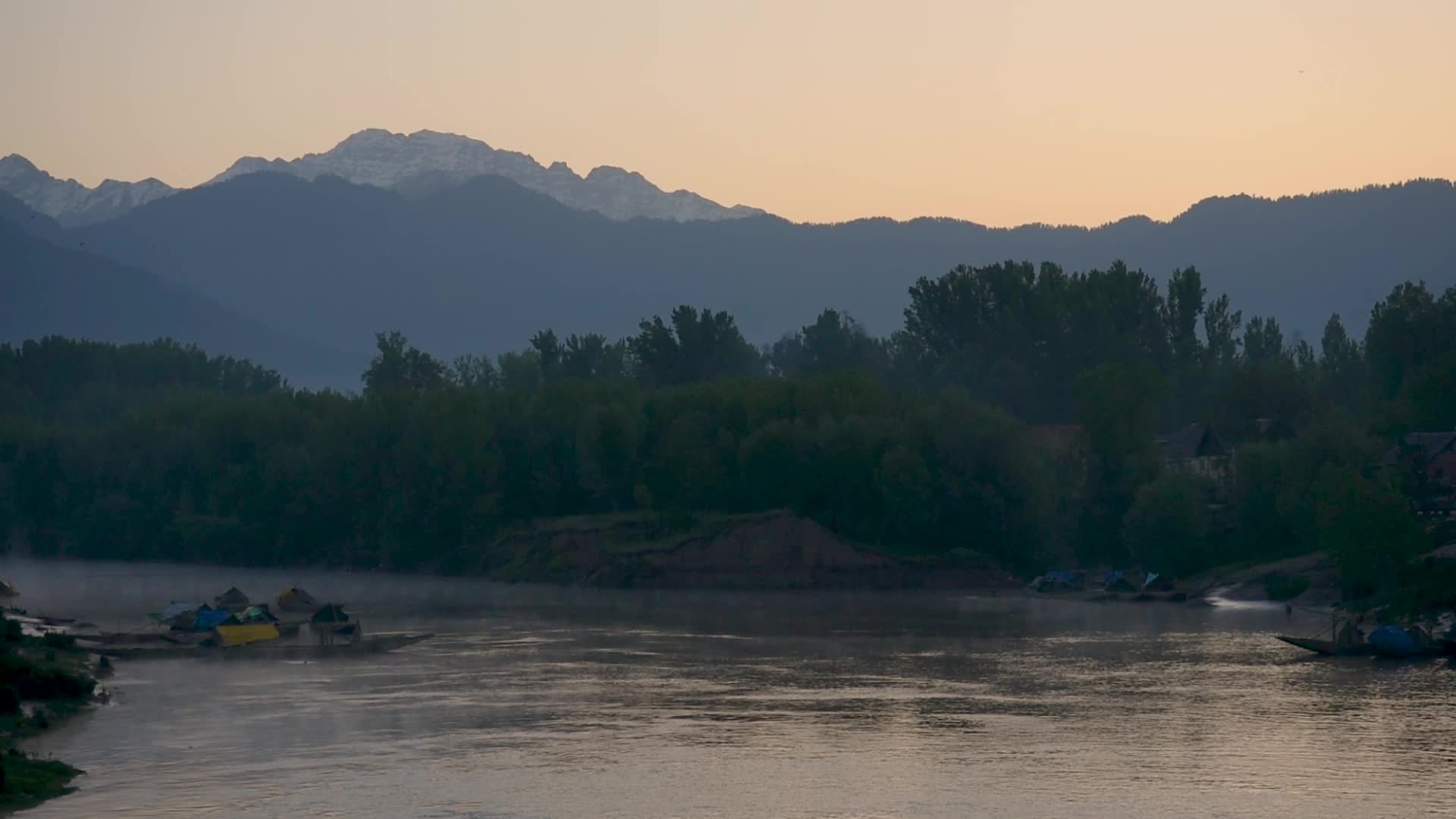River Jhelum flows with a backdrop of snow capped mountains during sunrise in South Kashmir.
