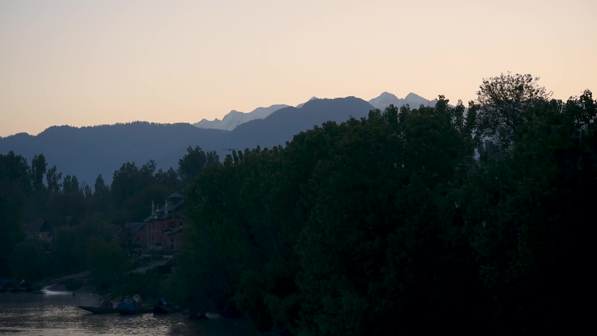 River Jhelum flows with a backdrop of snow capped mountains during sunrise in South Kashmir.