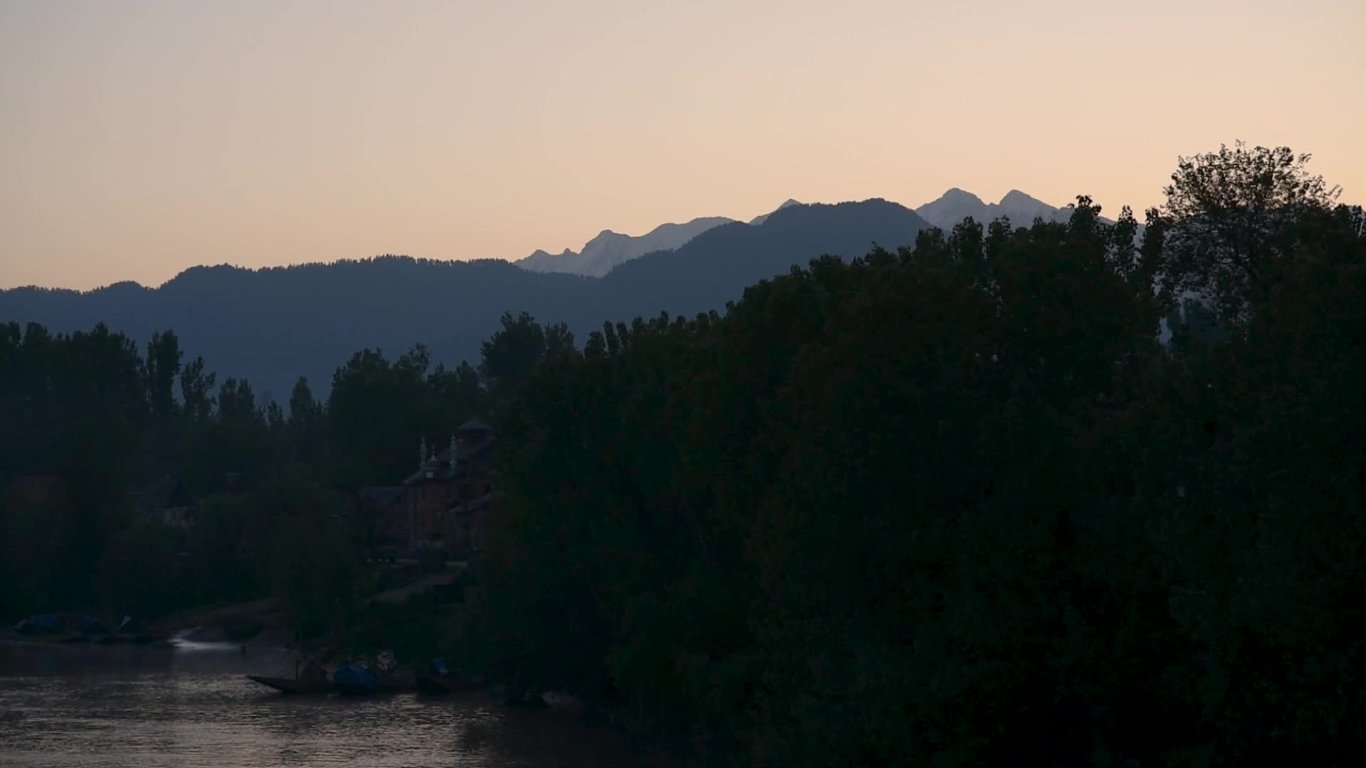River Jhelum flows with a backdrop of snow capped mountains during sunrise in South Kashmir.