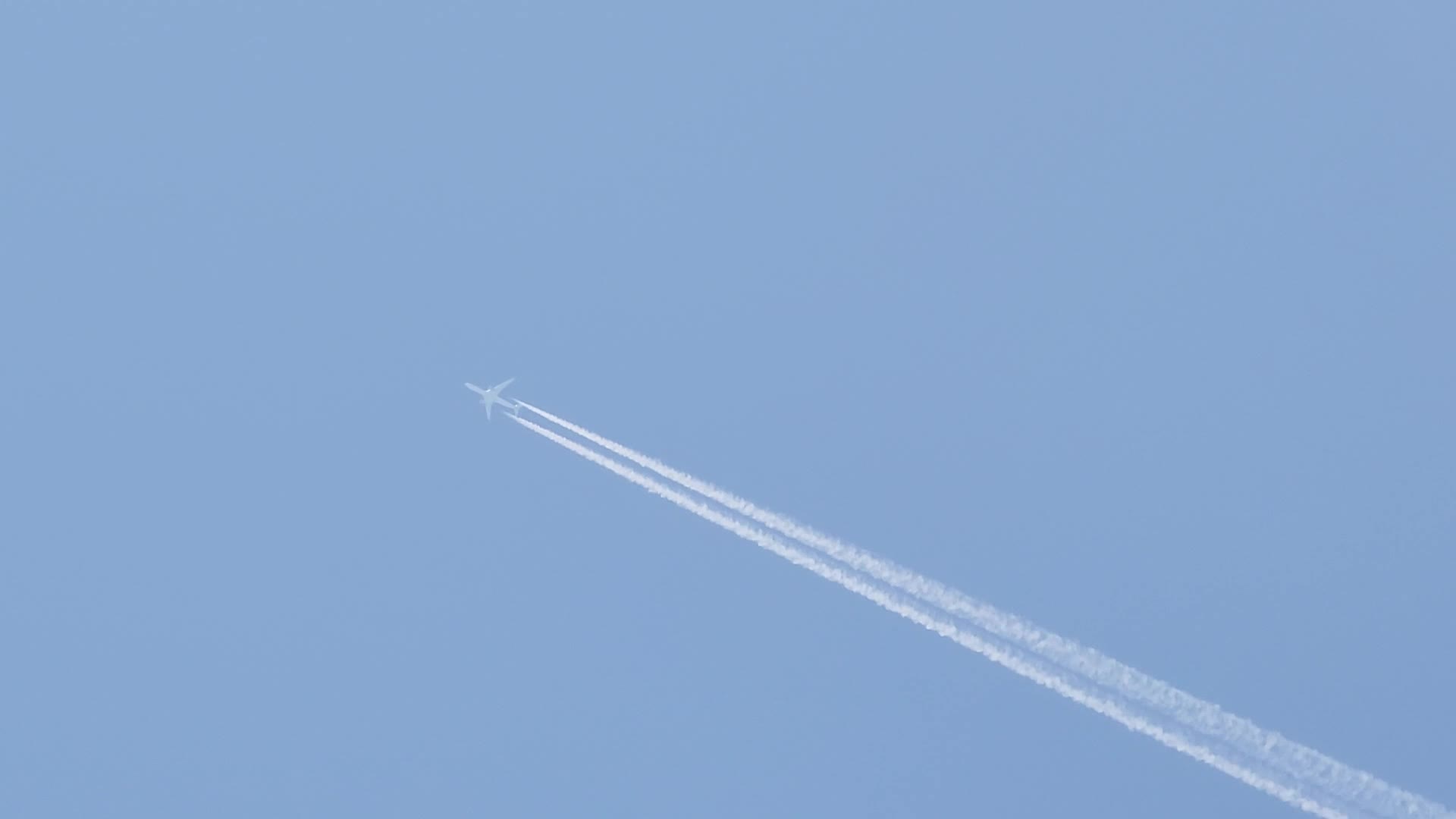 Airplane with contrails flying across a blue sky