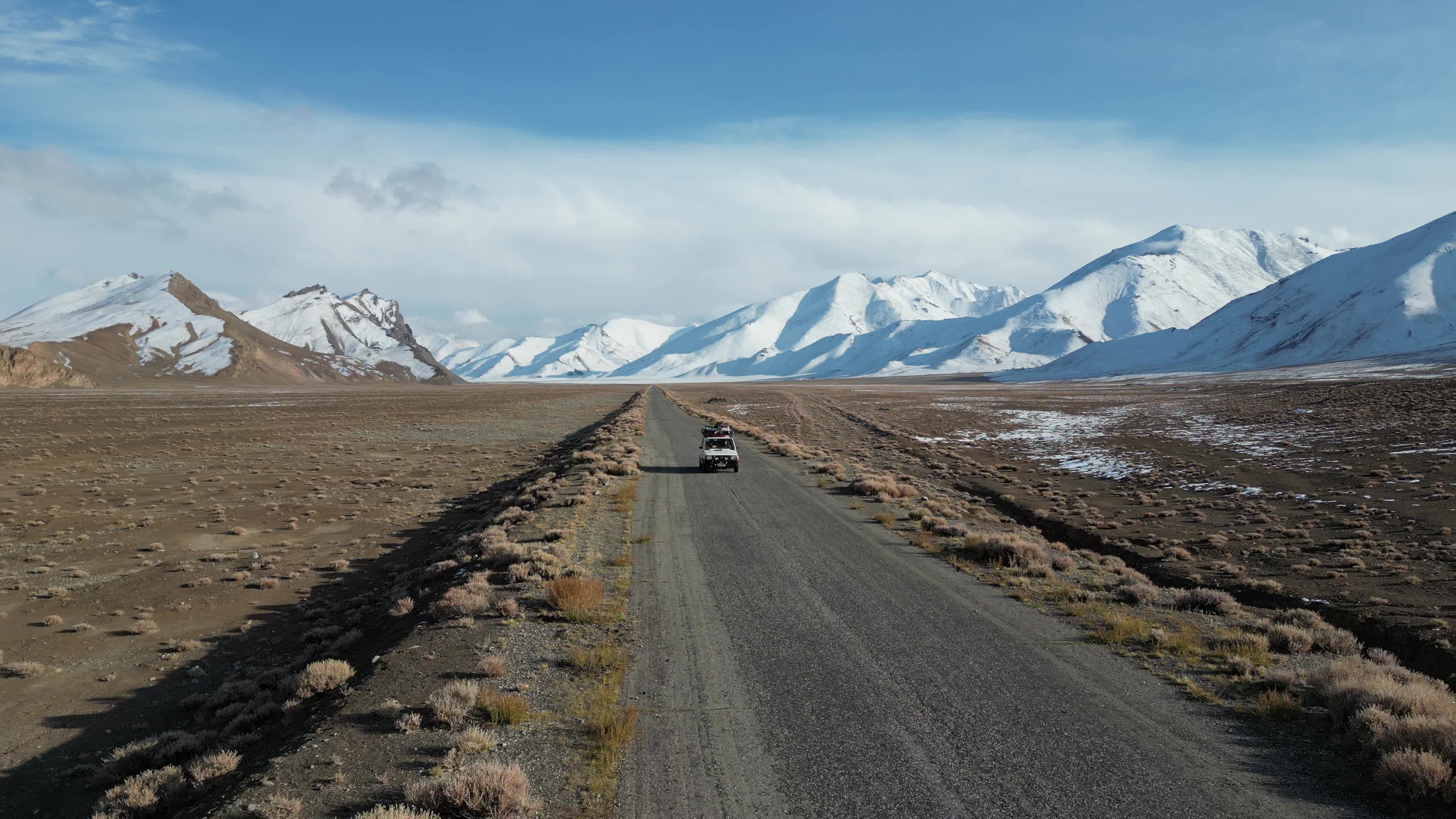 Drone shot of a small car driving on the pamir highway