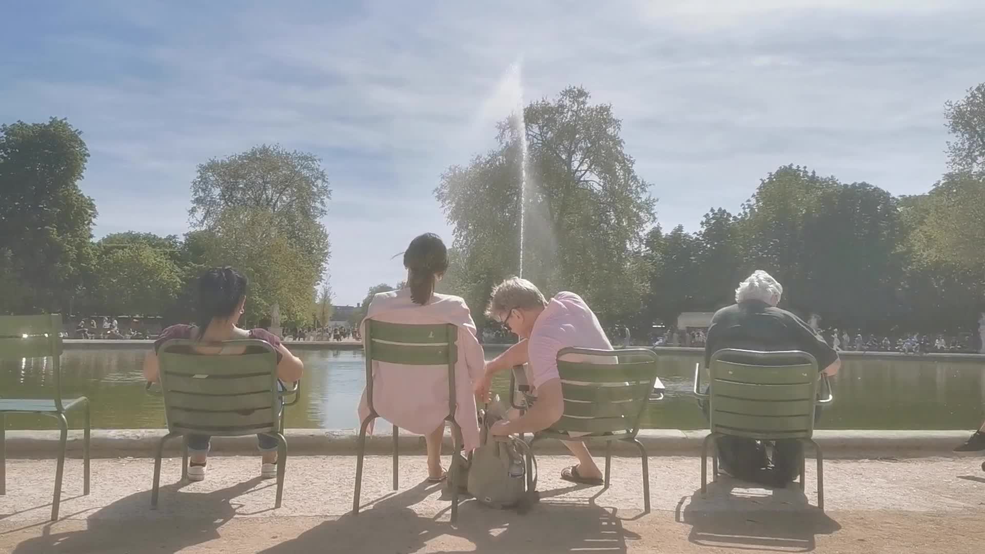 Tourists and Parisians enjoying the sun at the Tuileries Gardens and the Louvre in Paris 