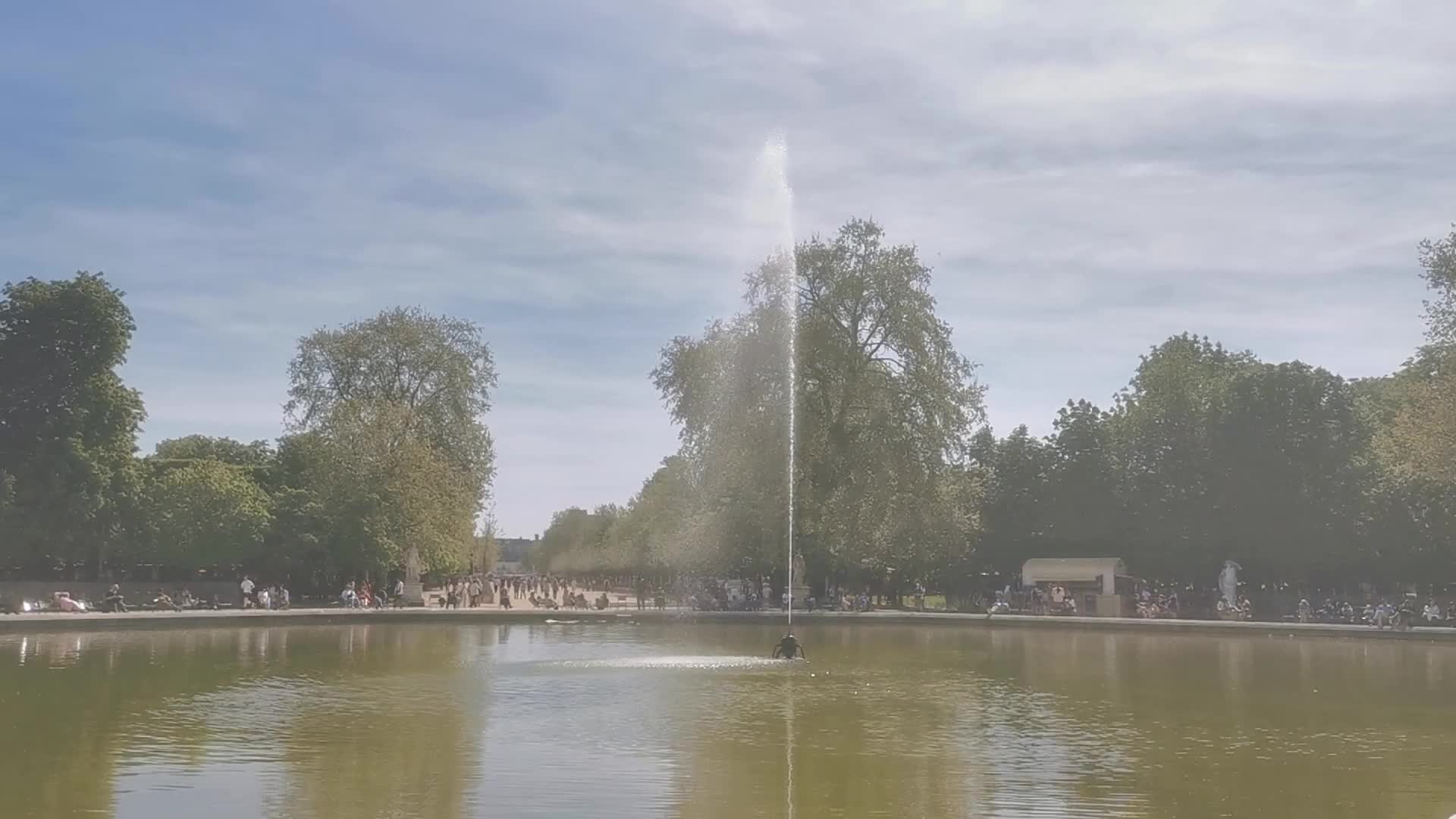 Tourists and Parisians enjoying the sun at the Tuileries Gardens and the Louvre in Paris 