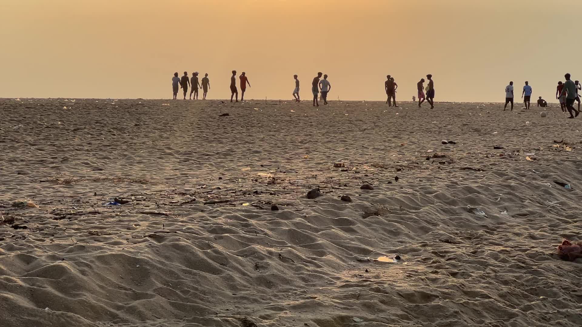Youth play a game of football by the ocean at sunset in Paruthiyoor