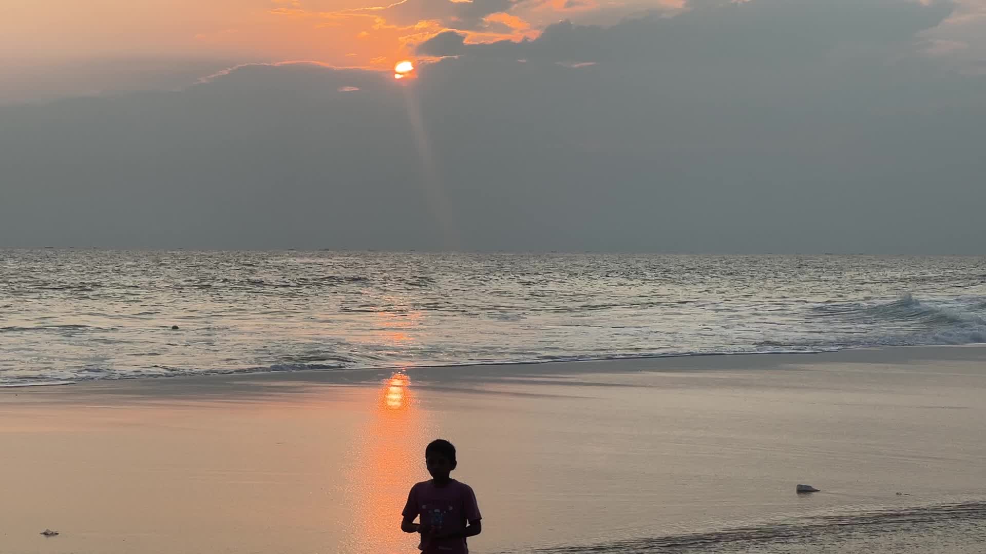 Youth play a game of football by the ocean at sunset in Paruthiyoor