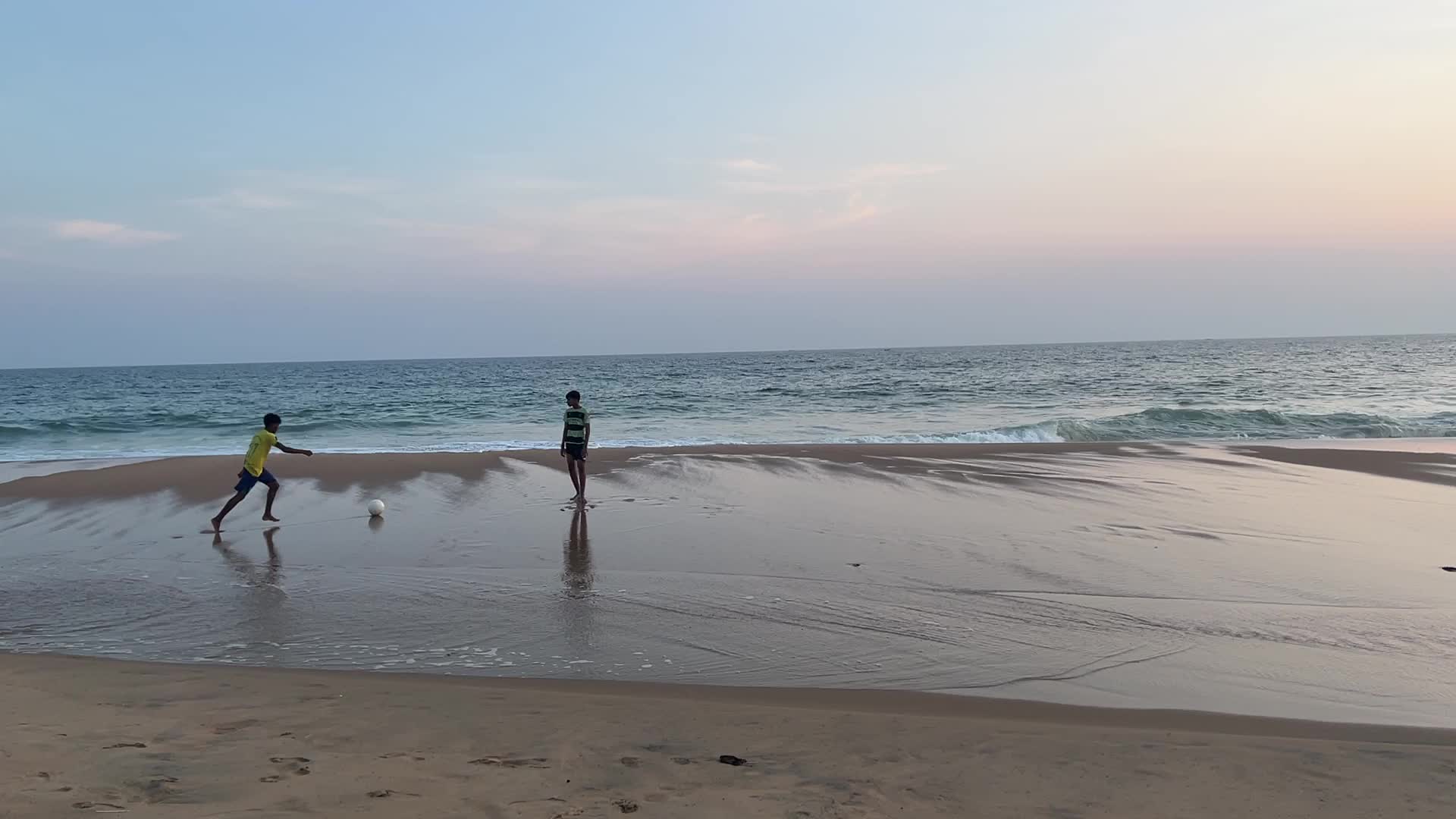 Youth play a game of football by the ocean at sunset in Paruthiyoor