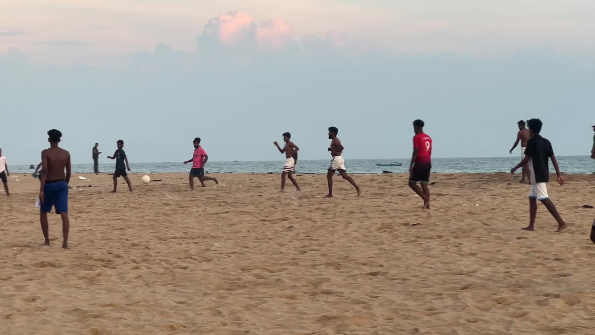 Youth play a game of football by the ocean at sunset in Paruthiyoor
