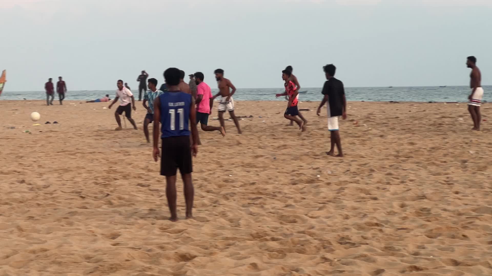 Youth play a game of football by the ocean at sunset in Paruthiyoor