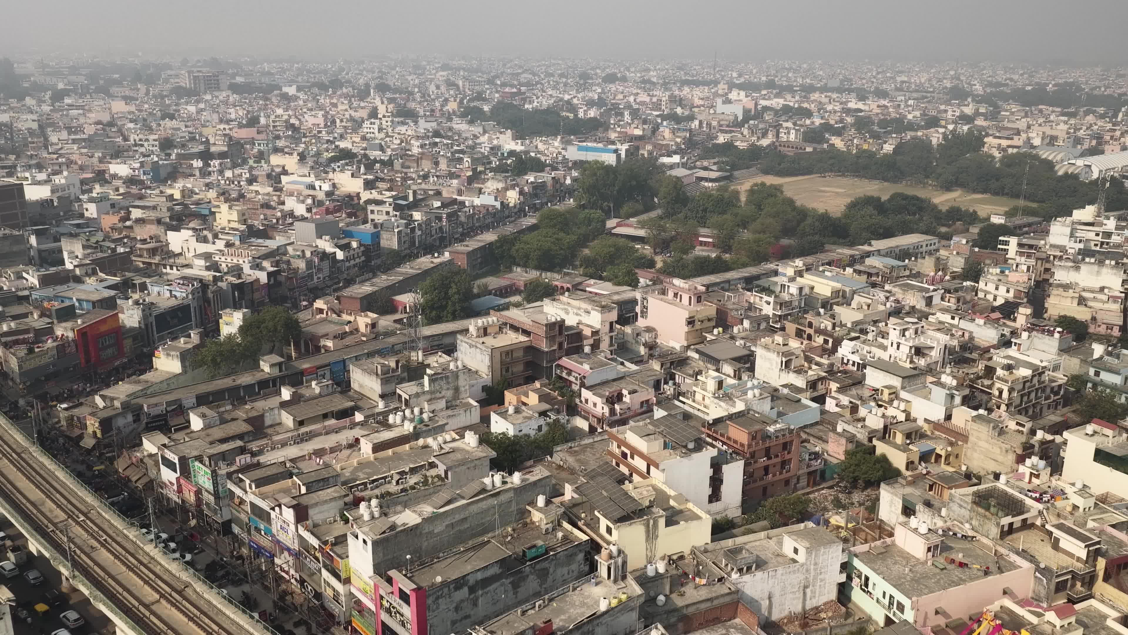 4K Aerial overpopulated View of Industrial & Residential Estate in Bahadurgarh City with elevated Metro train tracks and solar panels installed on the roof of the Metro Station, Harayana, India