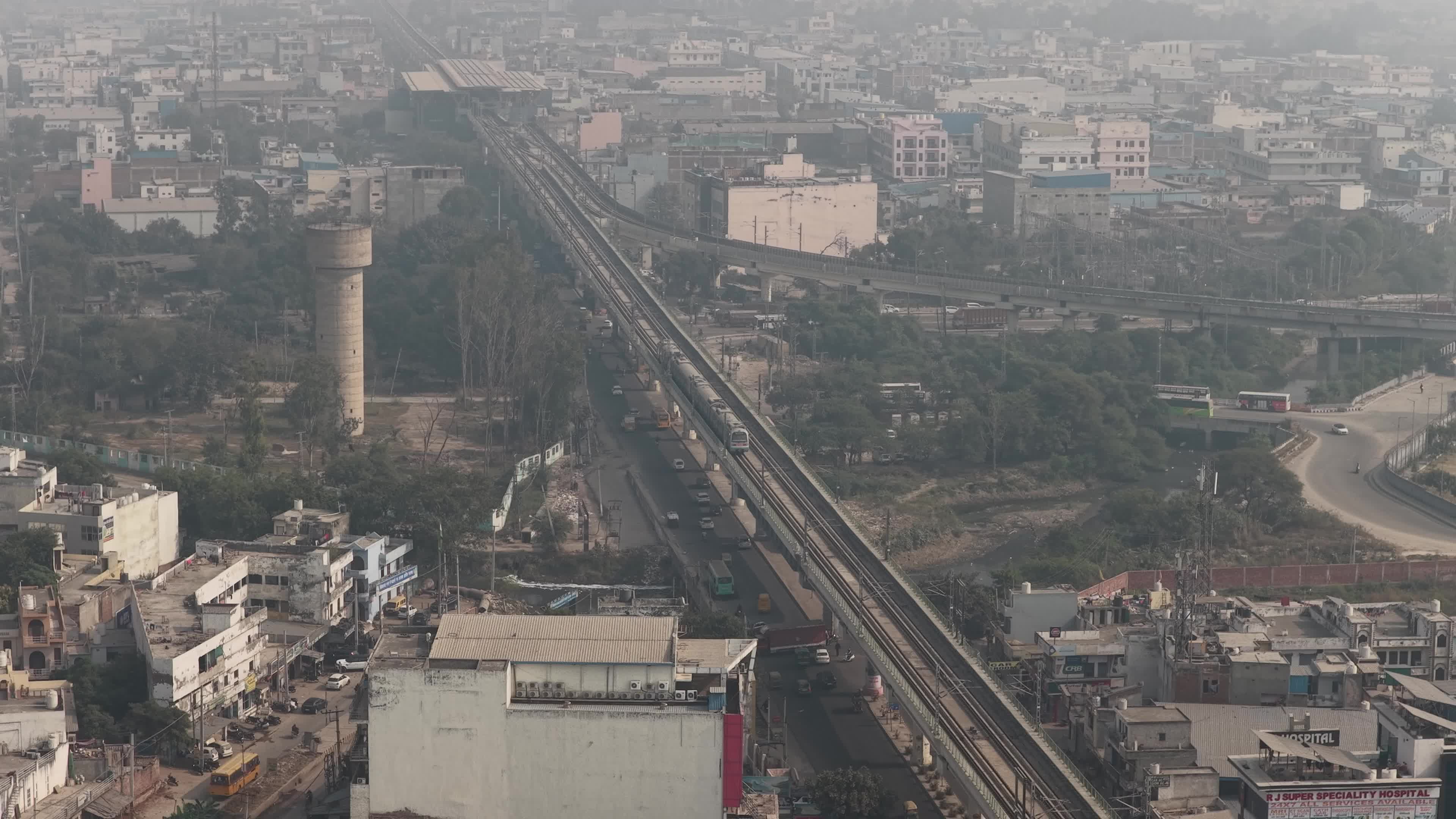 4K Aerial overpopulated View of Industrial & Residential Estate in Bahadurgarh City with elevated Metro train tracks and solar panels installed on the roof of the Metro Station, Haryana, India