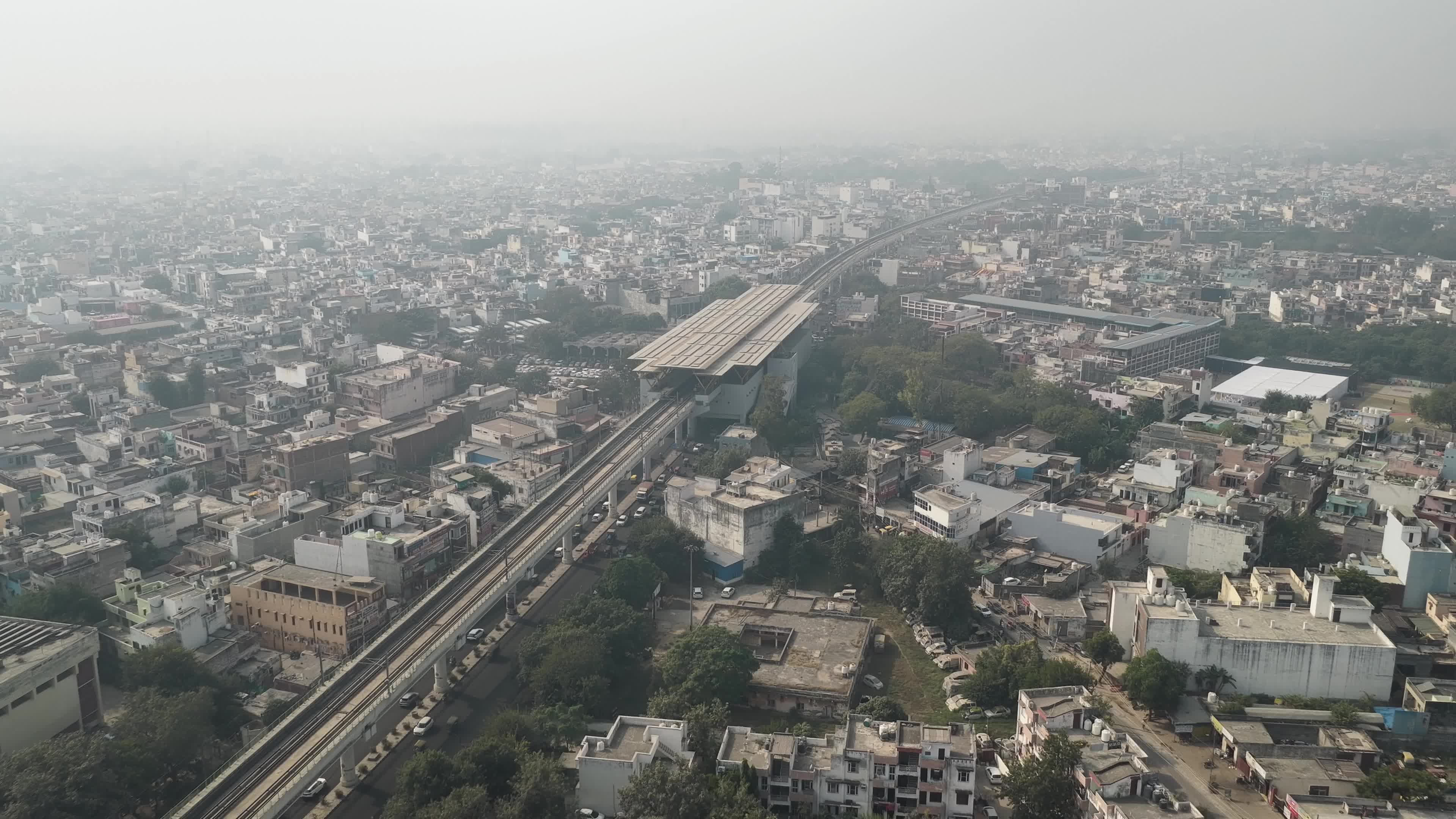 4K Aerial overpopulated View of Industrial & Residential Estate in Bahadurgarh City with elevated Metro train tracks and solar panels installed on the roof of the Metro Station, Haryana, India