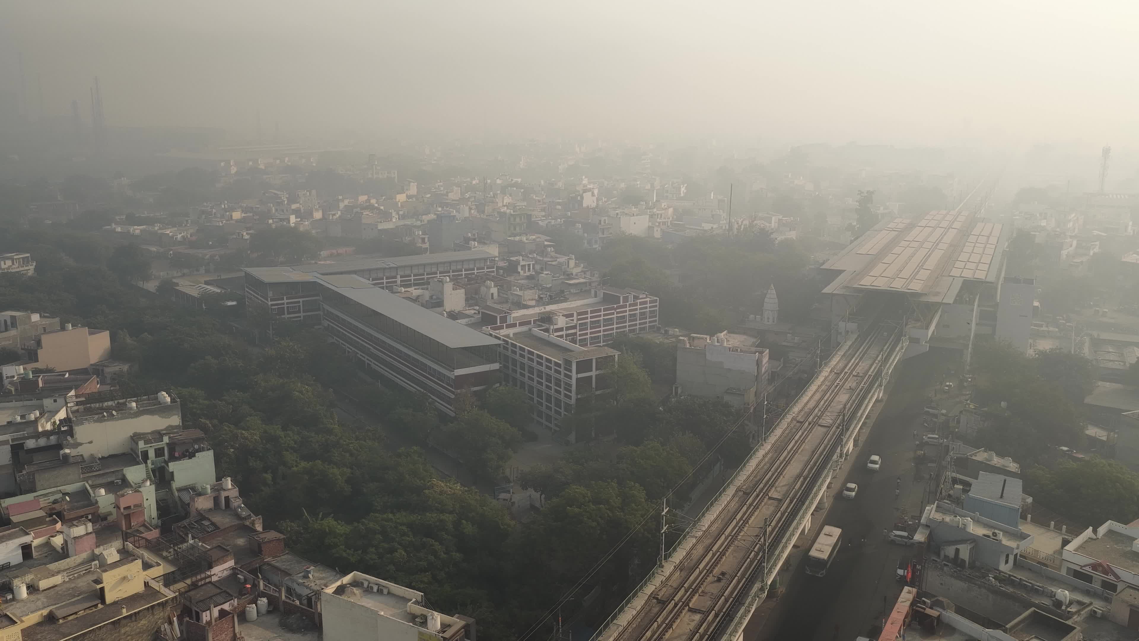 4K Aerial overpopulated View of Industrial & Residential Estate in Bahadurgarh City with elevated Metro train tracks and solar panels installed on the roof of the Metro Station, Haryana, India
