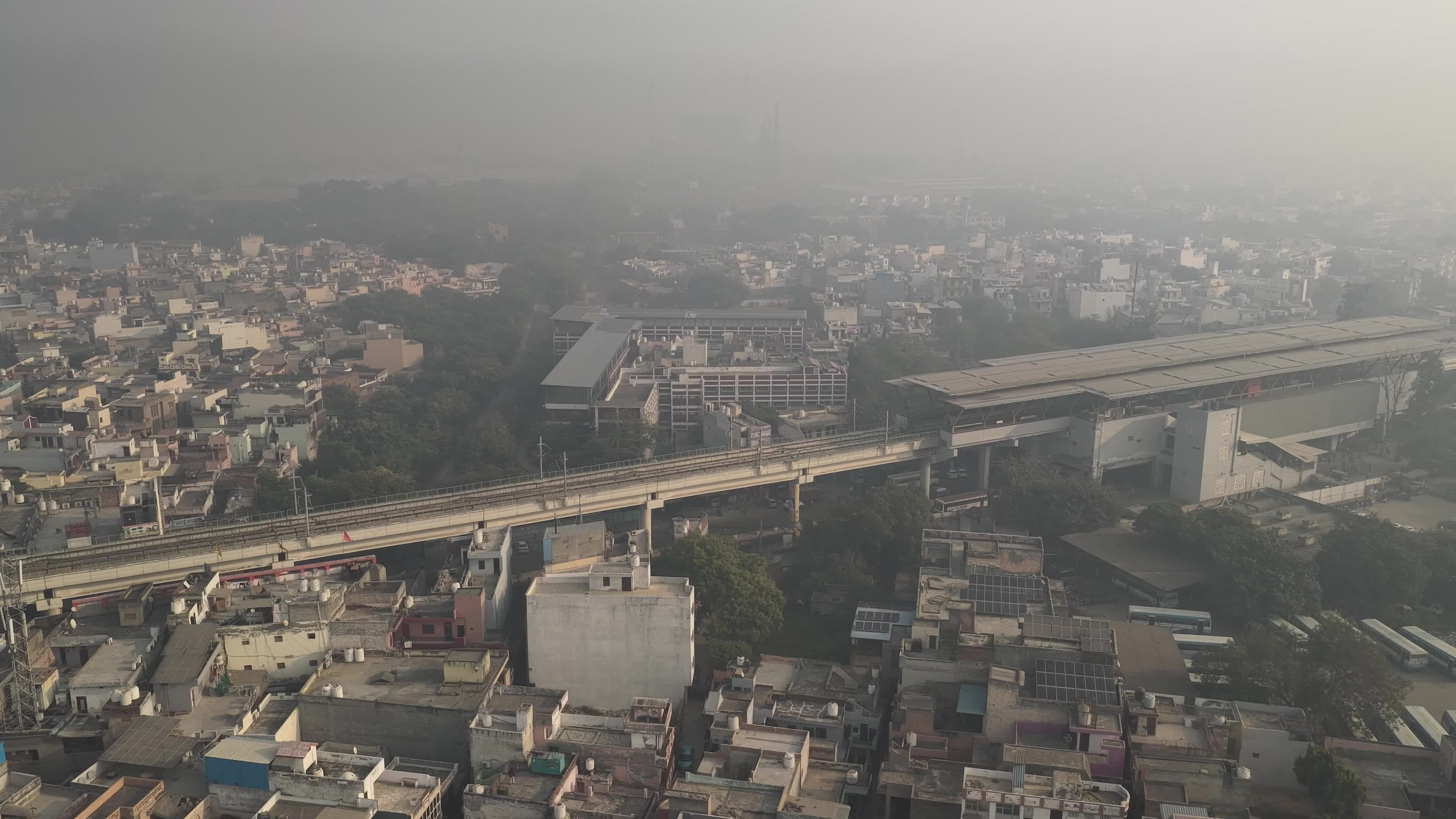 4K Aerial overpopulated View of Industrial & Residential Estate in Bahadurgarh City with elevated Metro train tracks and solar panels installed on the roof of the Metro Station, Haryana, India