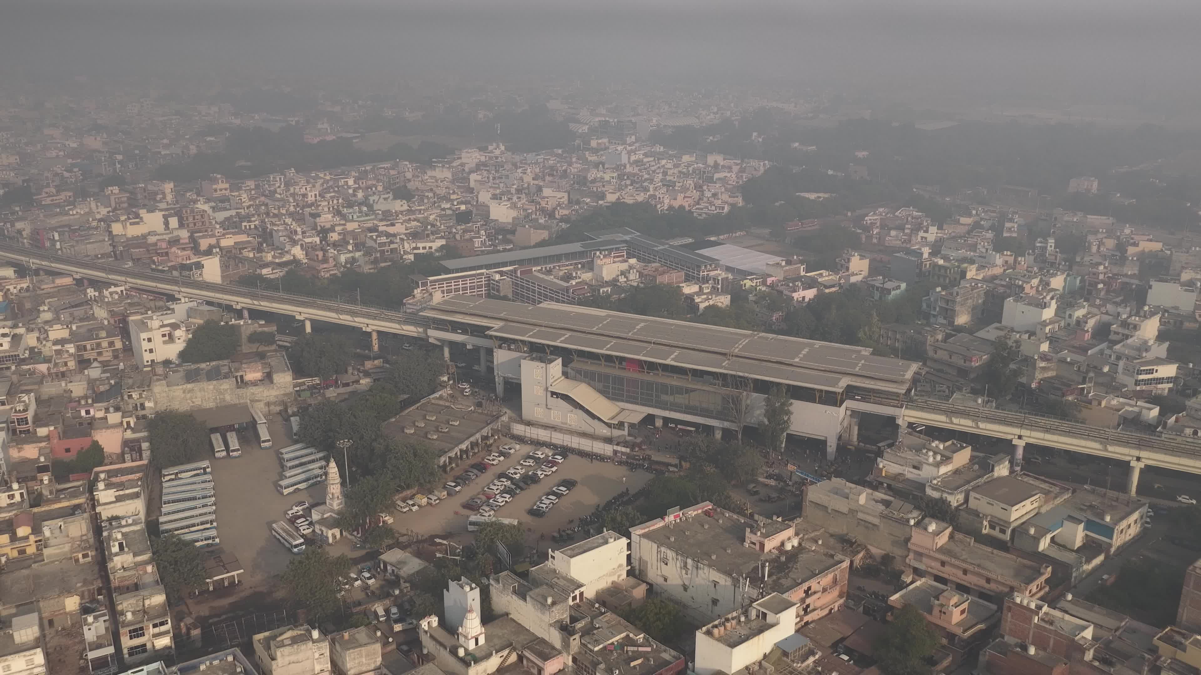 4K Aerial overpopulated View of Industrial & Residential Estate in Bahadurgarh City with elevated Metro train tracks and solar panels installed on the roof of the Metro Station, Haryana, India