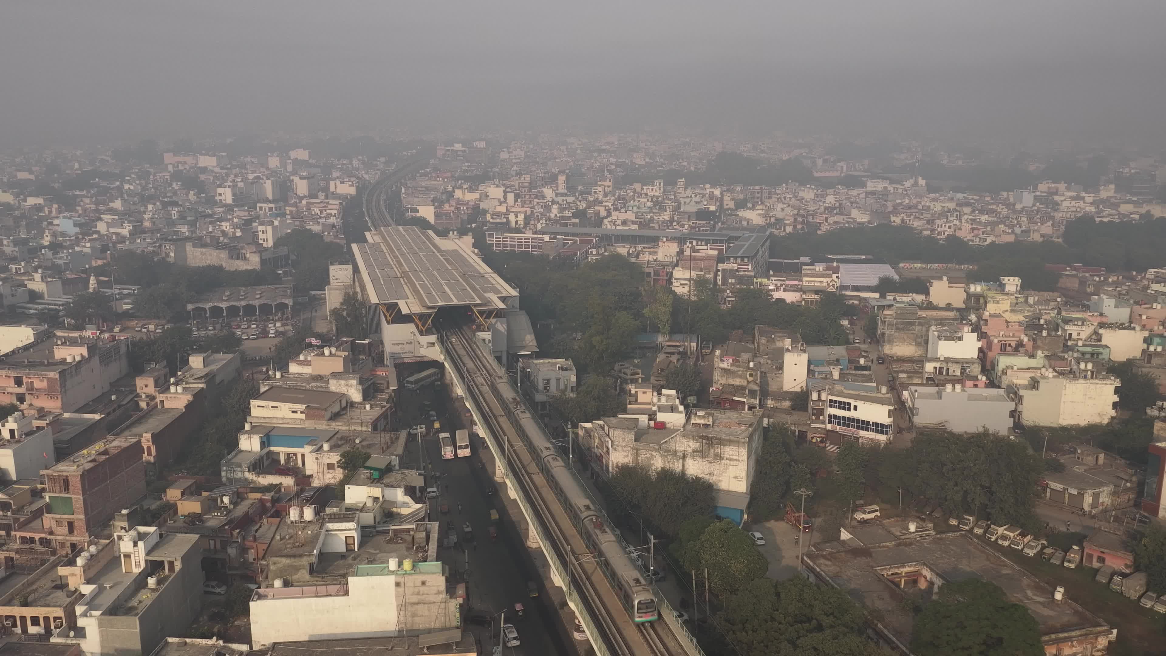4K Aerial overpopulated View of Industrial & Residential Estate in Bahadurgarh City with elevated Metro train tracks and solar panels installed on the roof of the Metro Station, Haryana, India