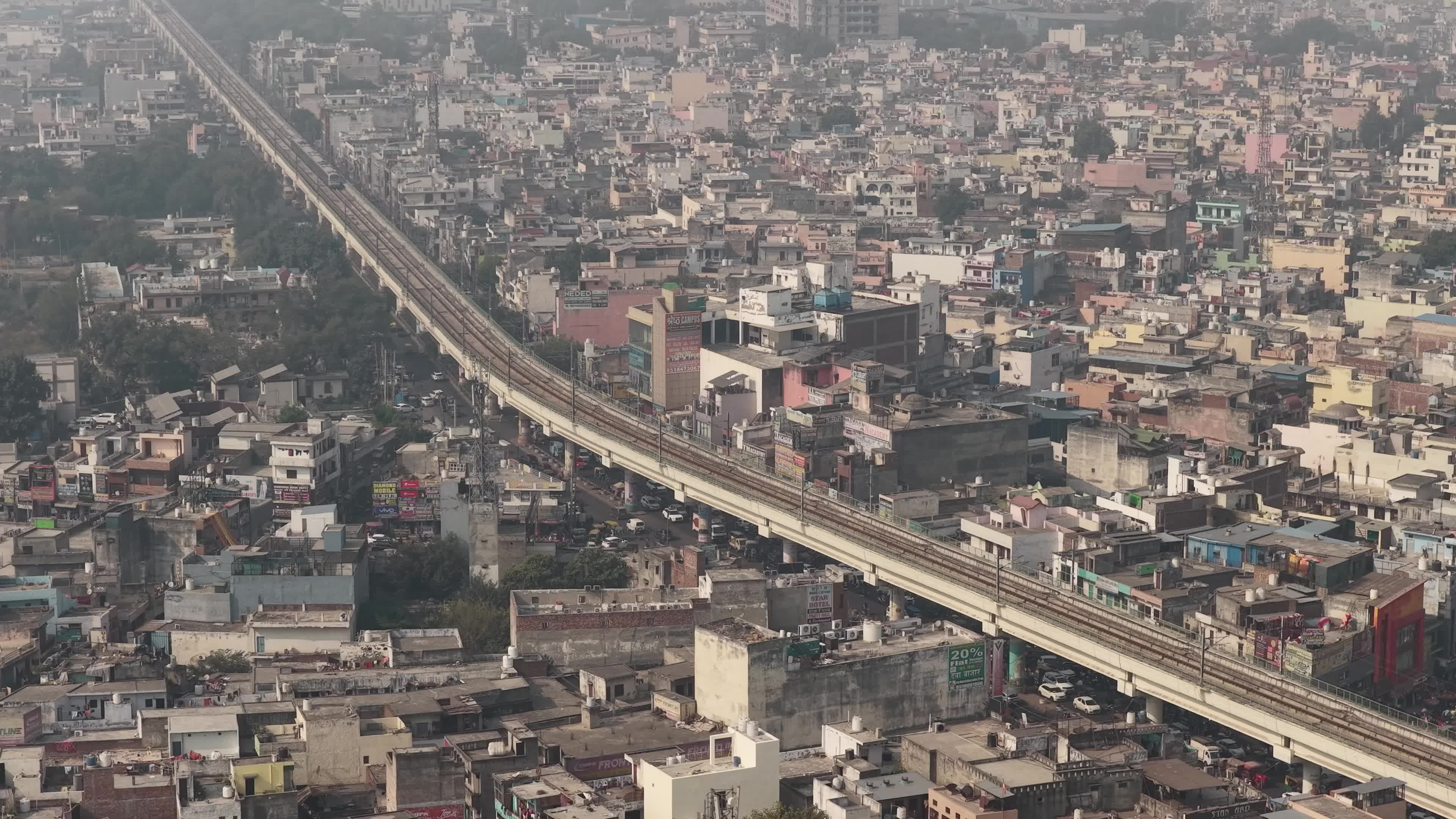 4K Aerial overpopulated View of Industrial & Residential Estate in Bahadurgarh City with elevated Metro train tracks and solar panels installed on the roof of the Metro Station, Haryana, India