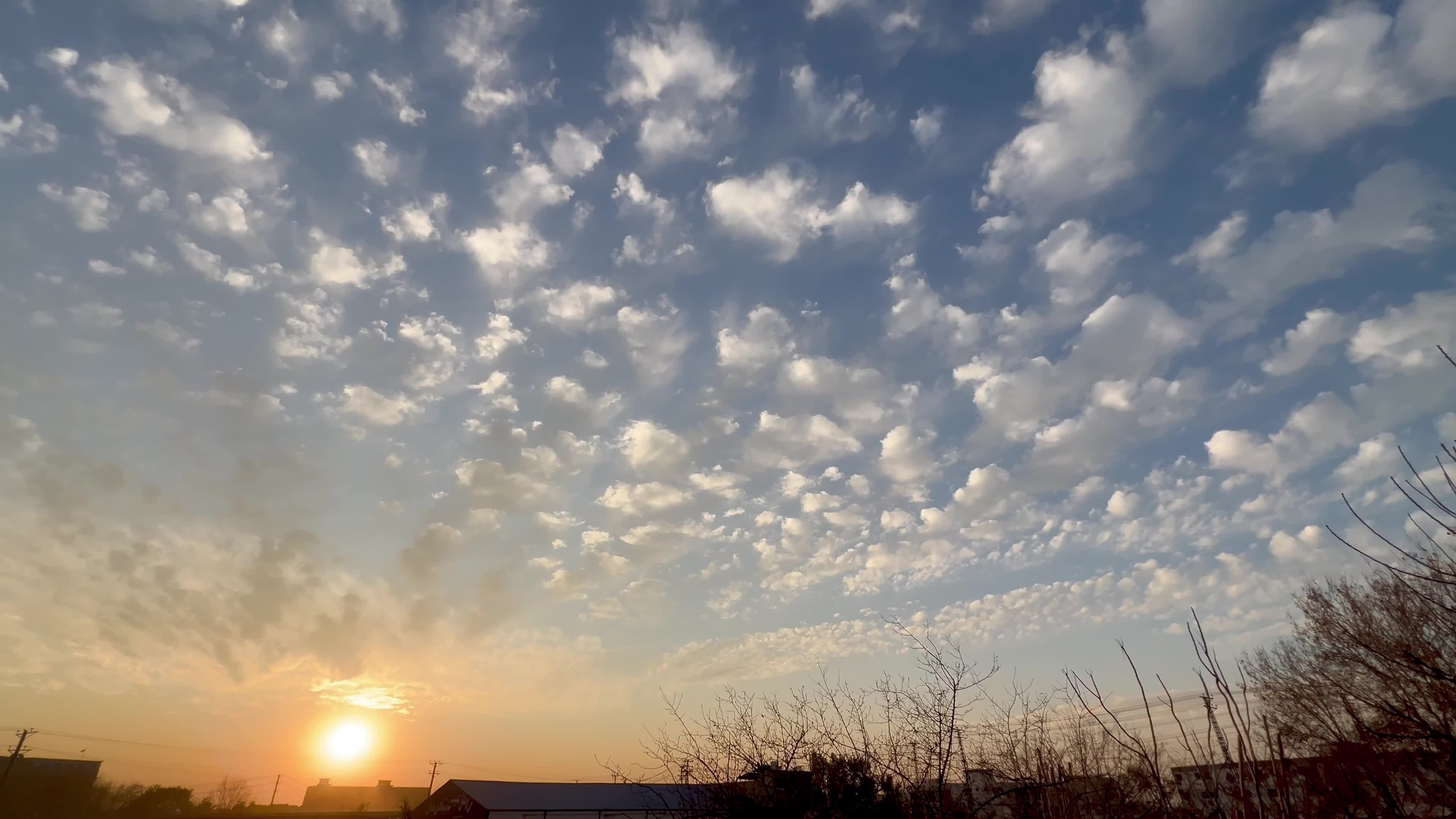 Sun sets beneath scattered clouds