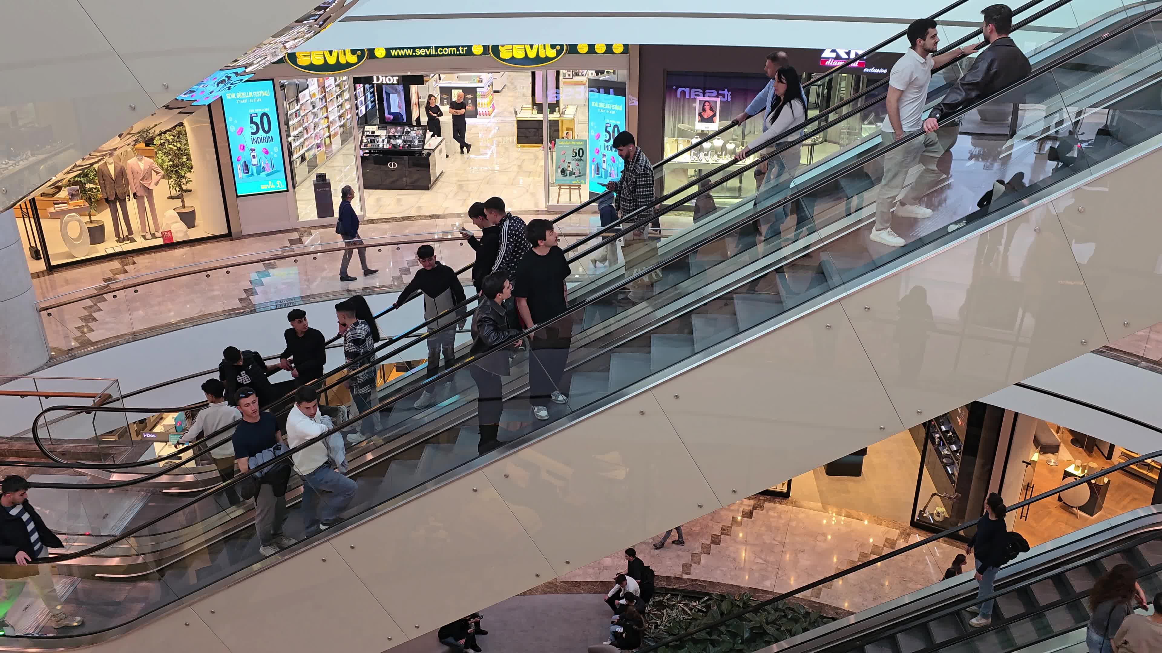 A diverse crowd of people navigating the escalators and walkways of a large, multi-level commercial center