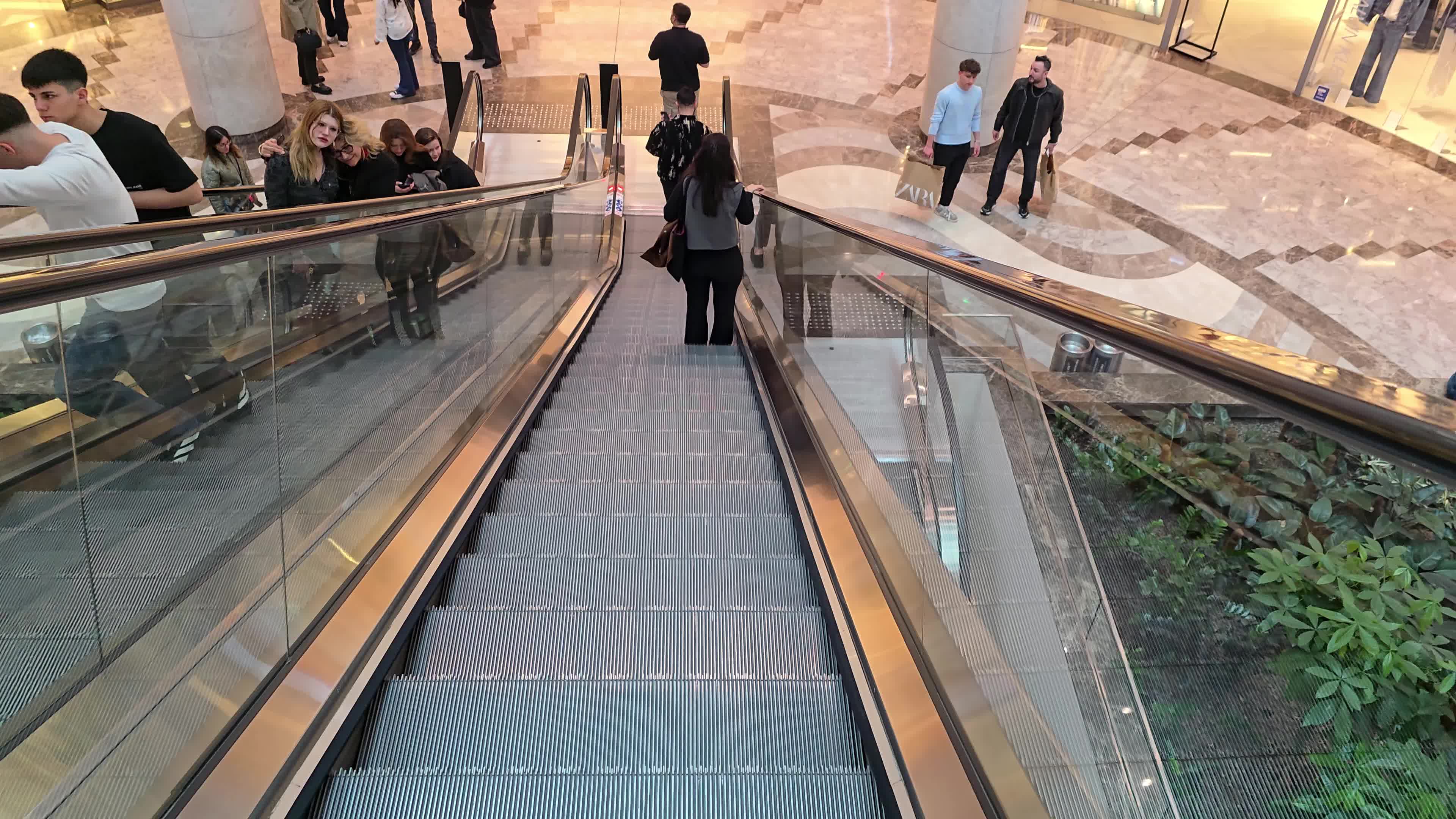 A diverse crowd of people navigating the escalators and walkways of a large, multi-level commercial center