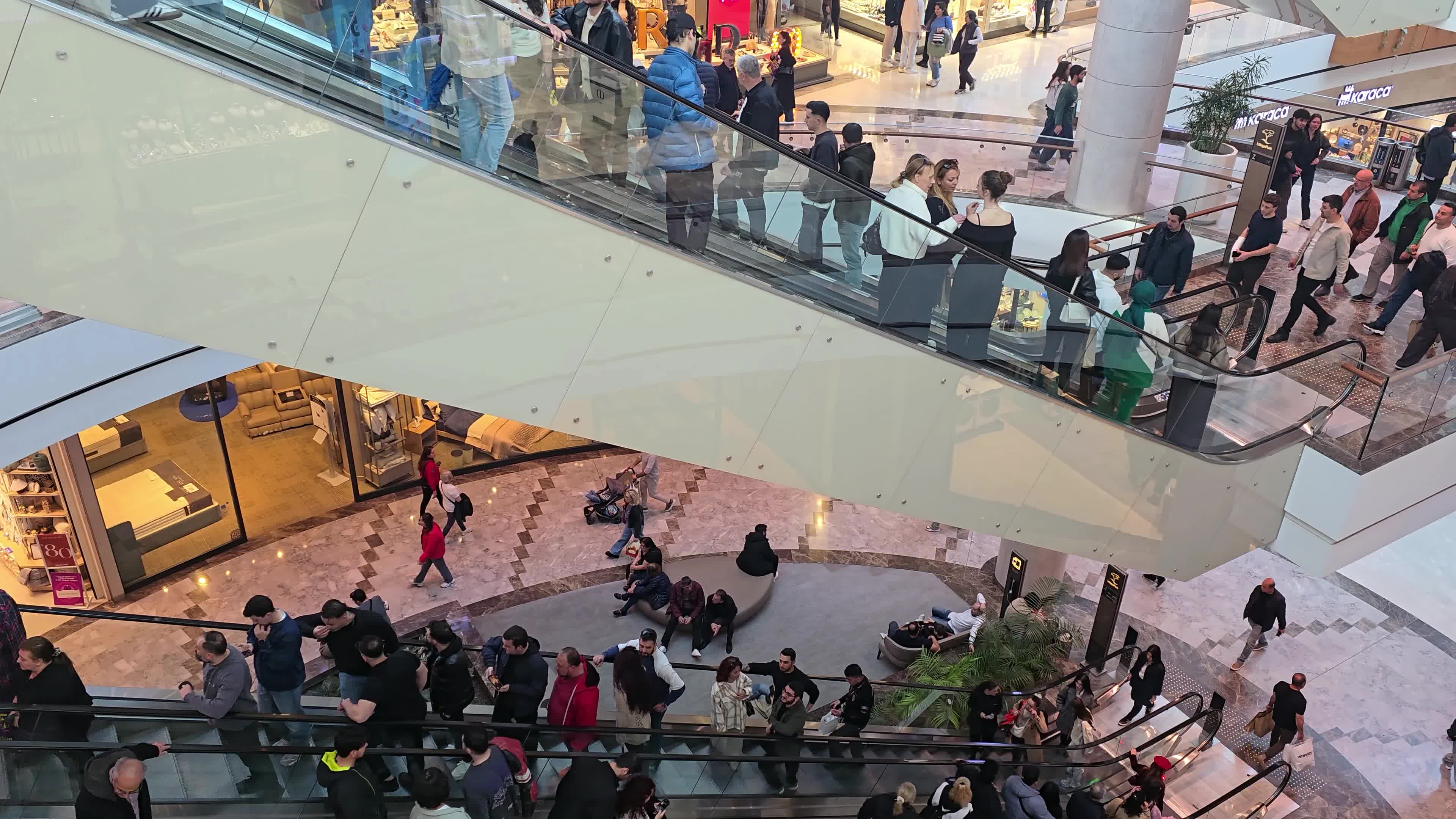 A diverse crowd of people navigating the escalators and walkways of a large, multi-level commercial center