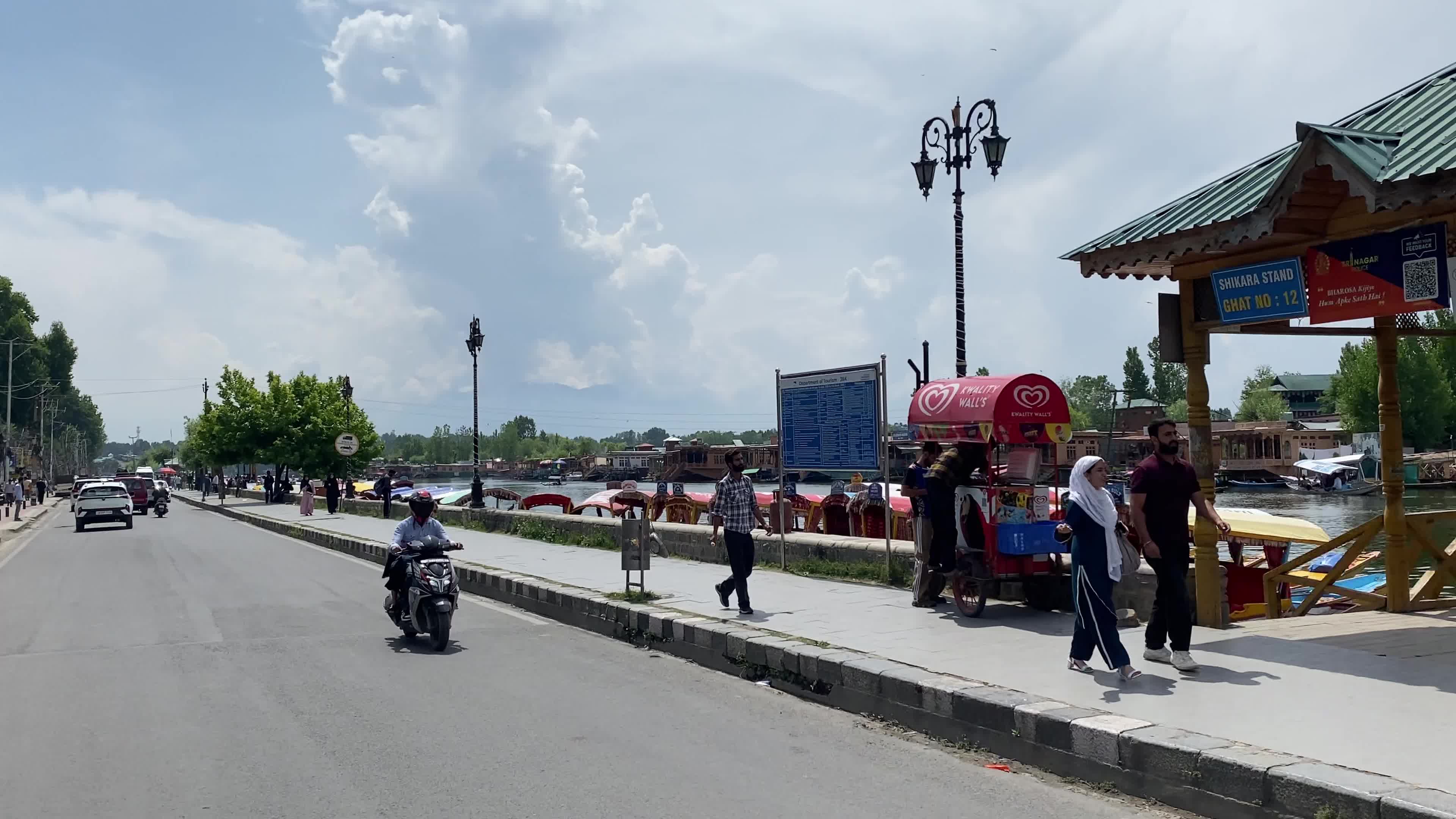 Vehicles move while people walk along the banks of Dal Lake on a sunny summer day in Srinagar, India.