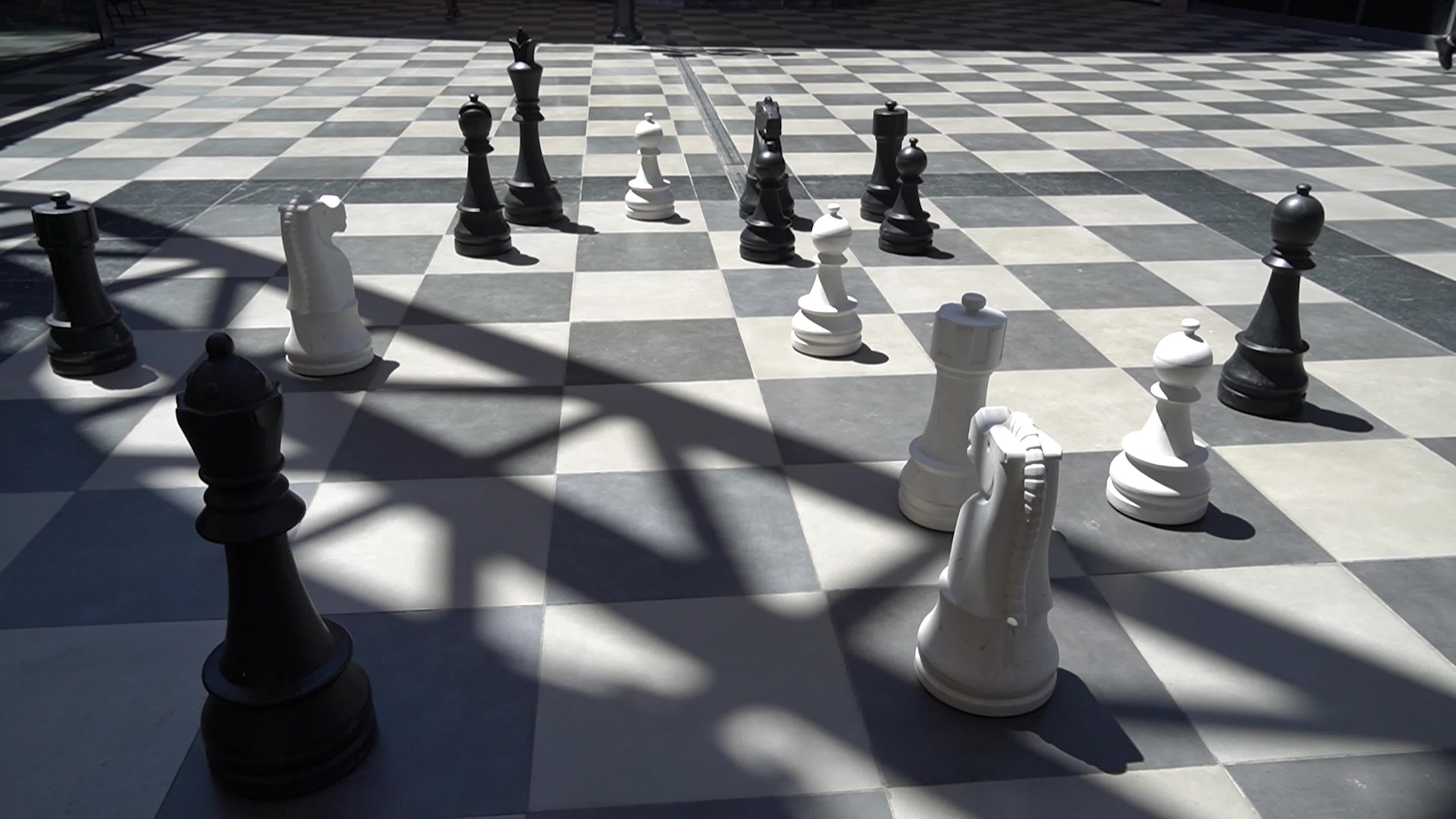 Giant outdoor chess set with oversized black and white pieces on a checkered pavement