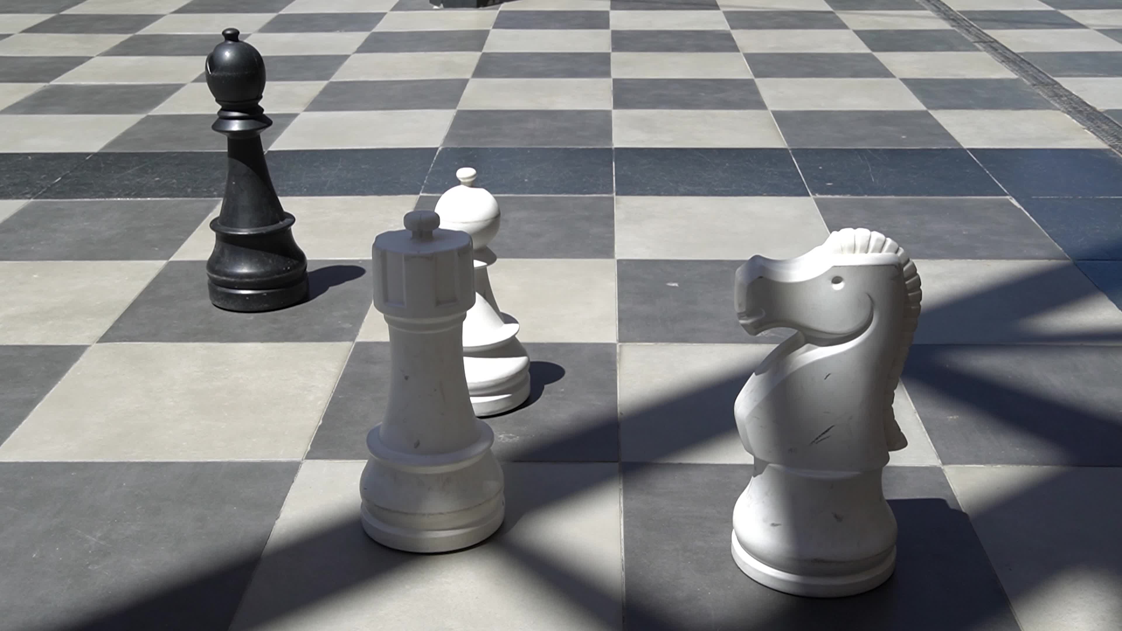 Giant outdoor chess set with oversized black and white pieces on a checkered pavement