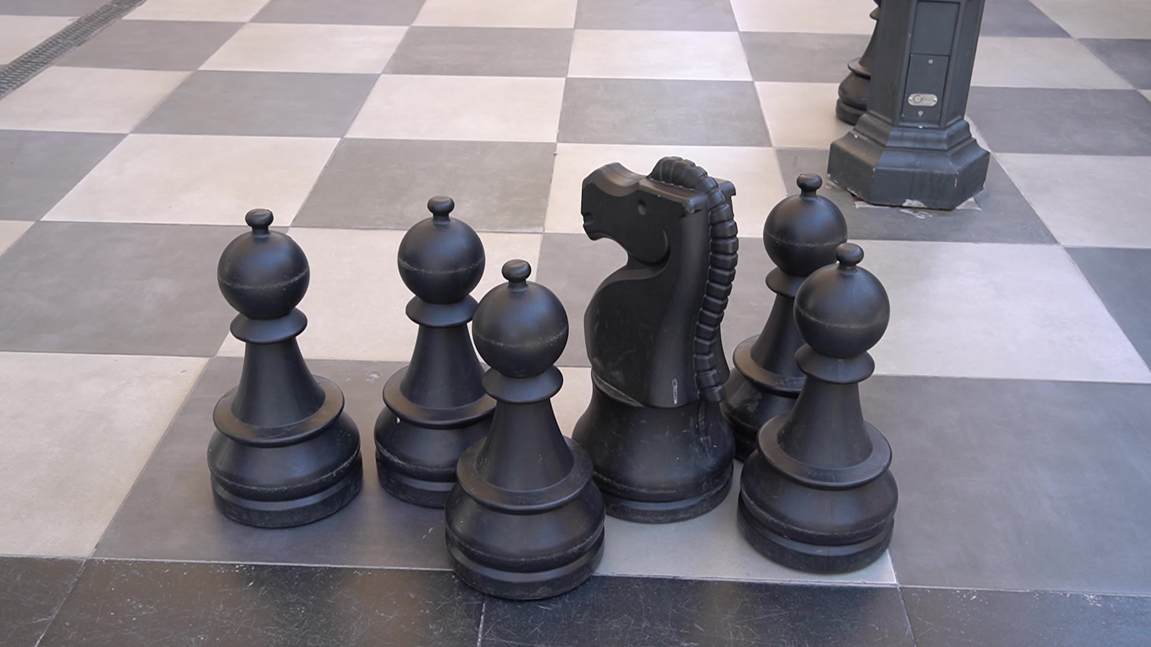 Giant outdoor chess set with oversized black and white pieces on a checkered pavement