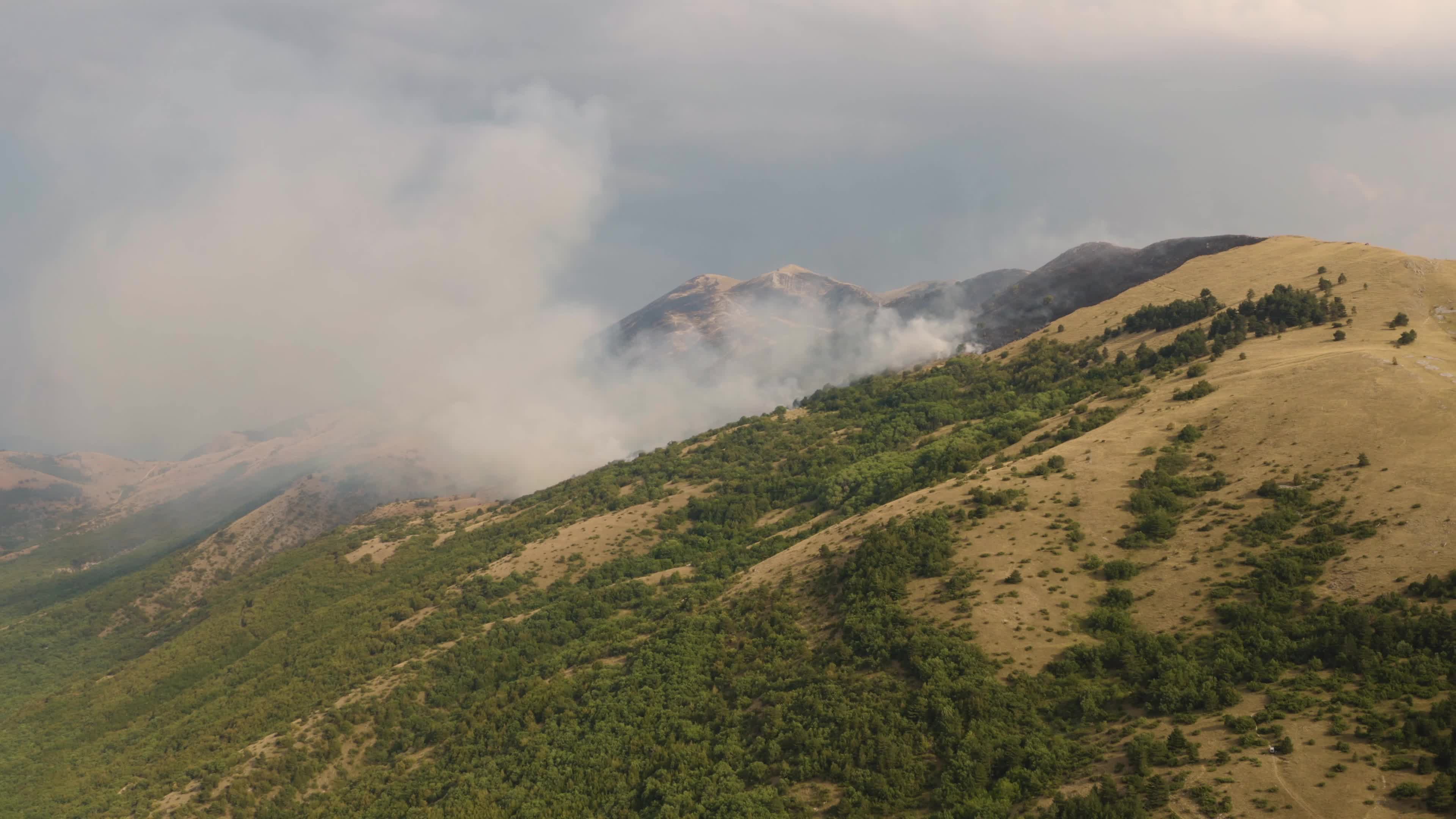 Aerial drone view of mountain wildfire and smoke plume in Italy climate change emergency