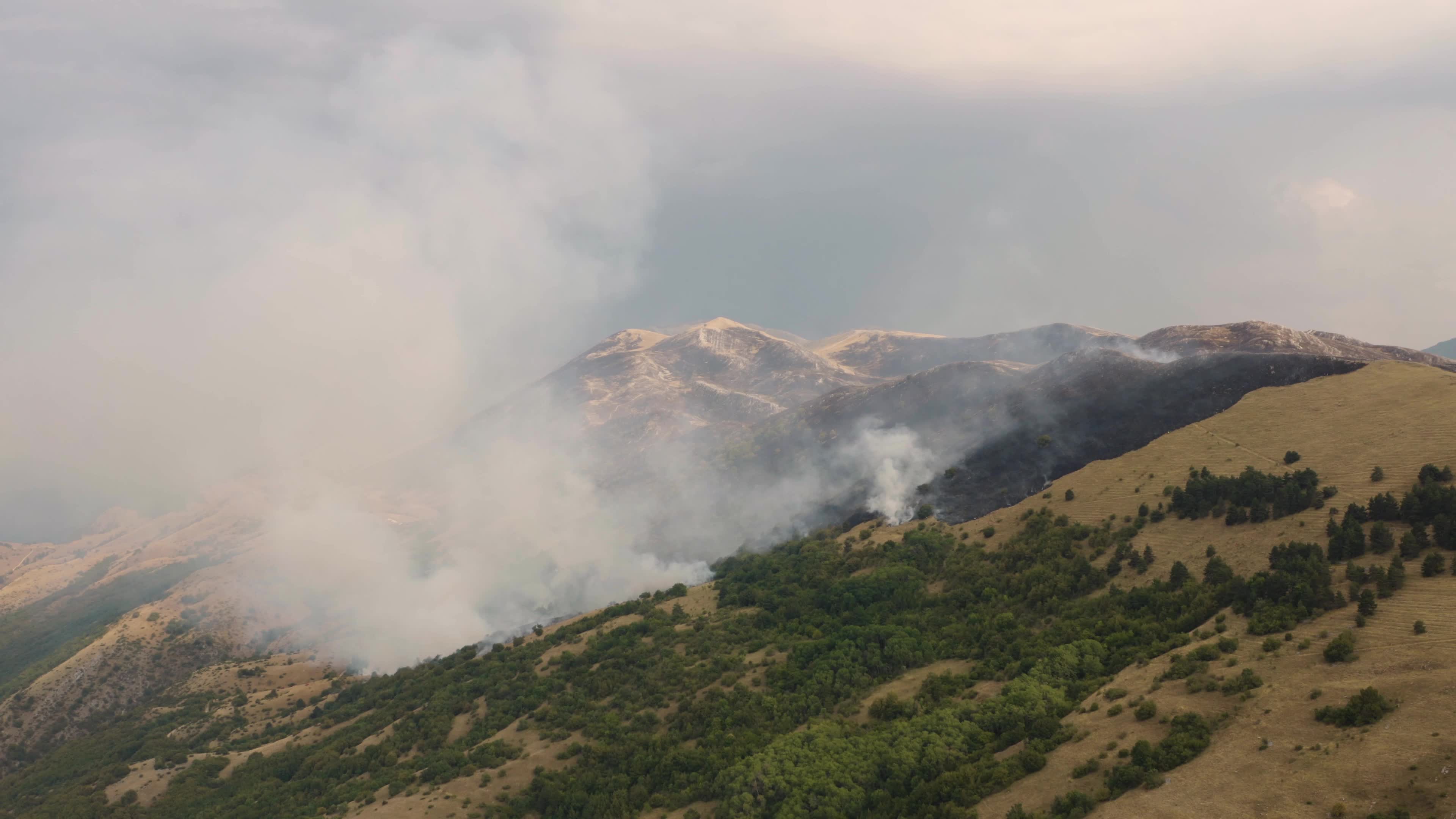 Aerial drone view of mountain wildfire and smoke plume in Italy climate change emergency