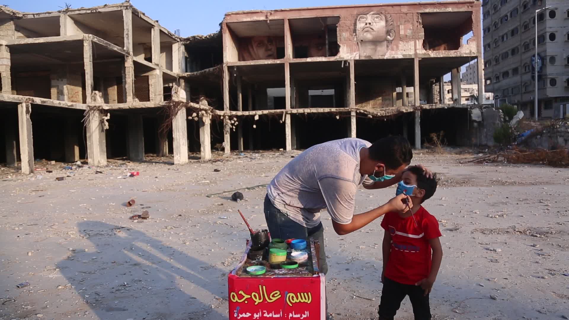 Palestinian artist draws a mask to childs in Gaza