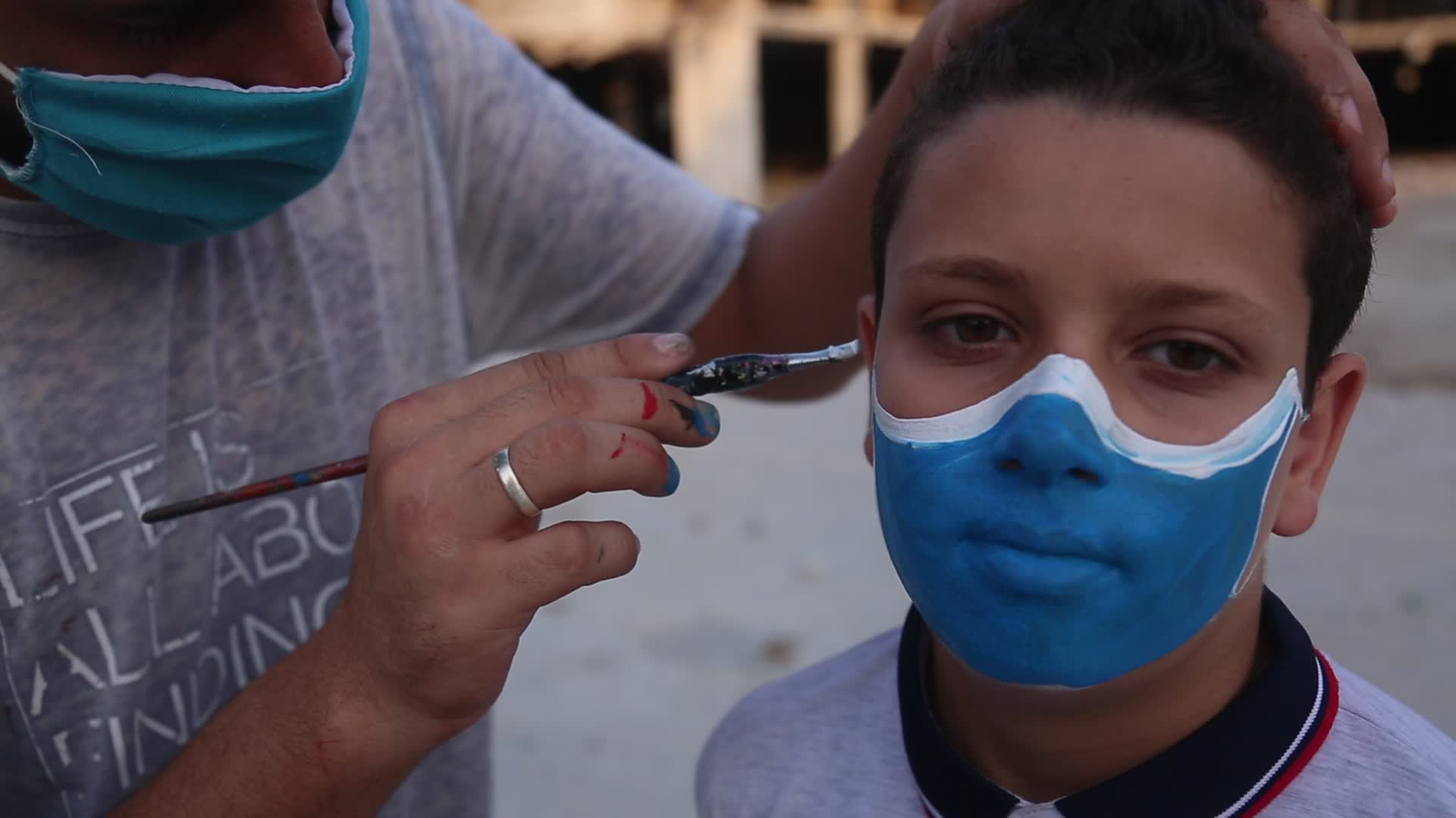 Palestinian artist draws a mask to childs in Gaza