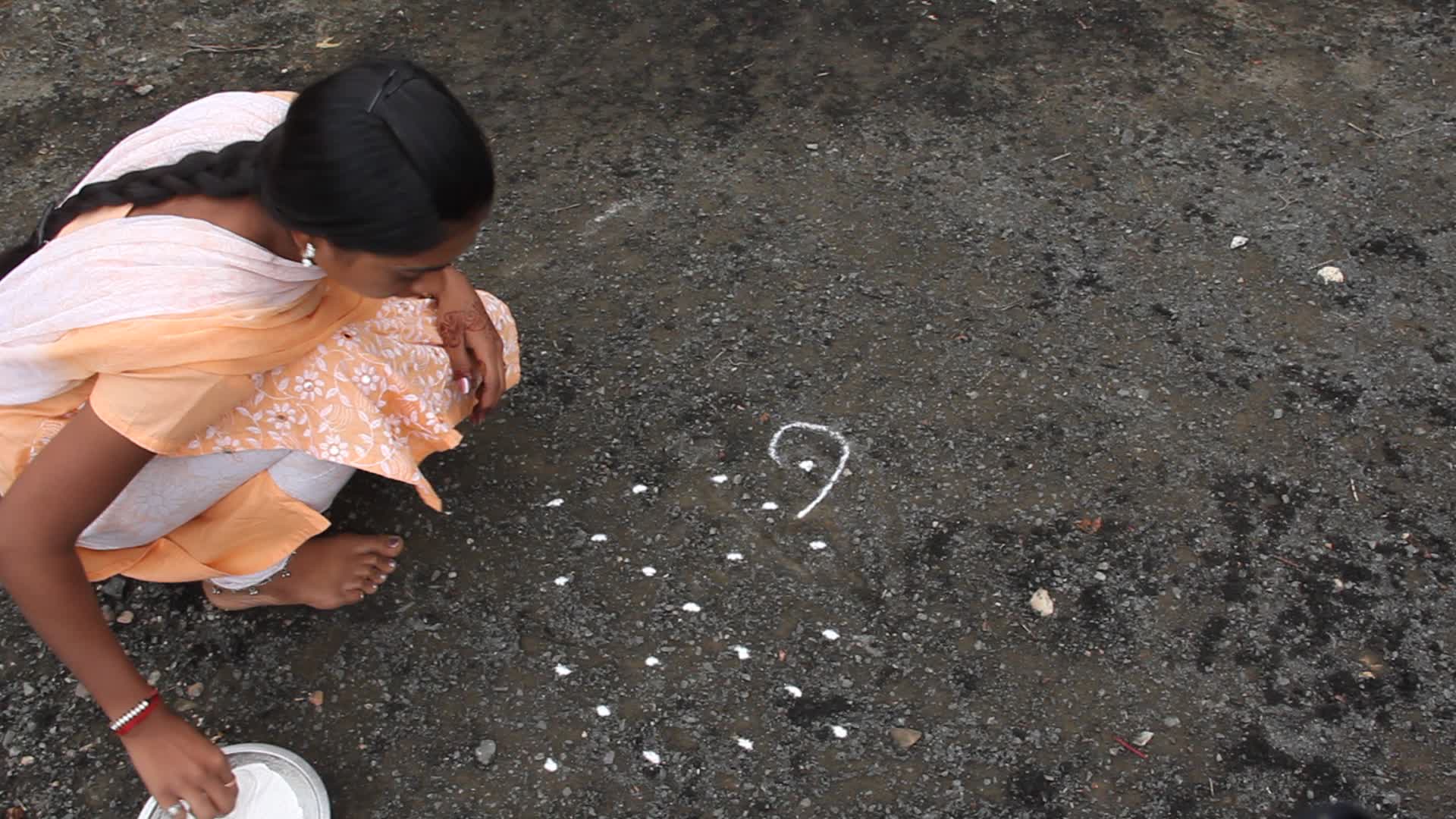Girl draws a rangoli design in front of a temple
